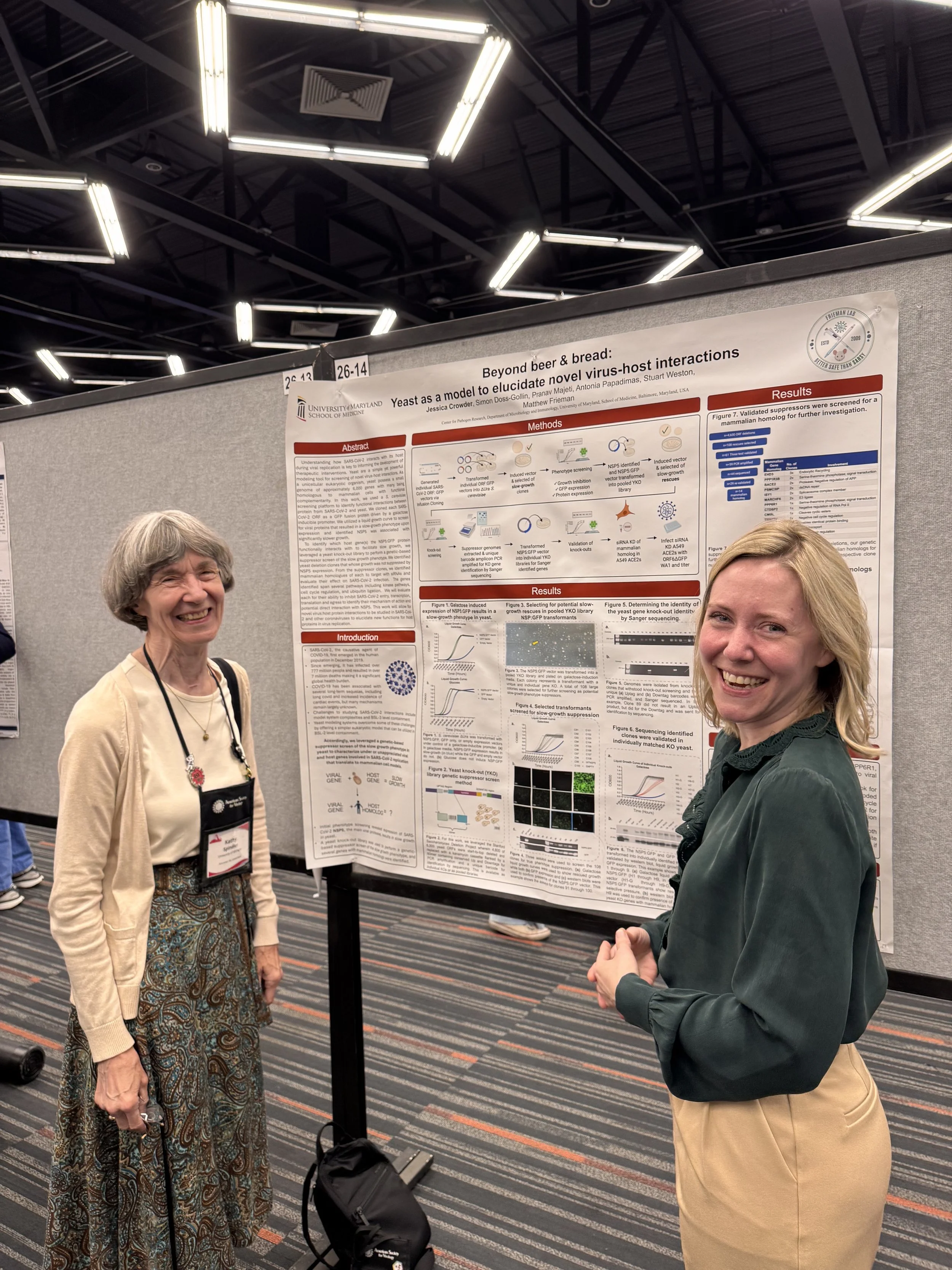 Two women standing in front of a scientific research poster at a conference, smiling and looking at the camera.