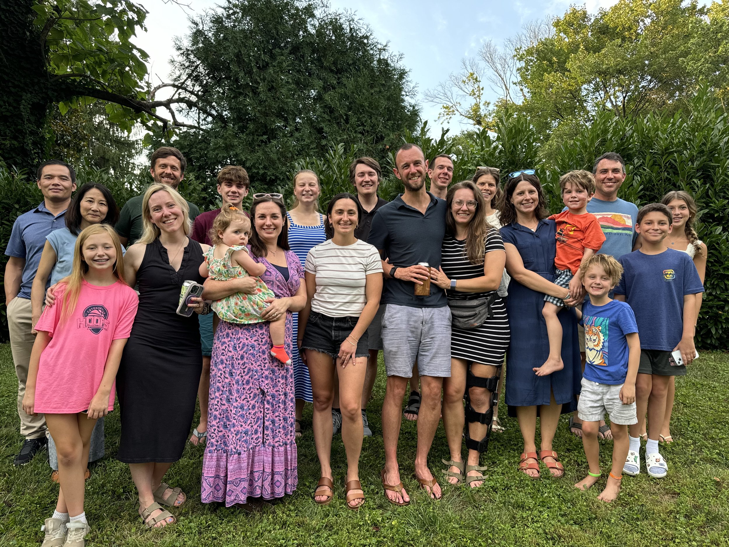 A large group of people gathered outdoors in front of greenery, smiling for a photo.