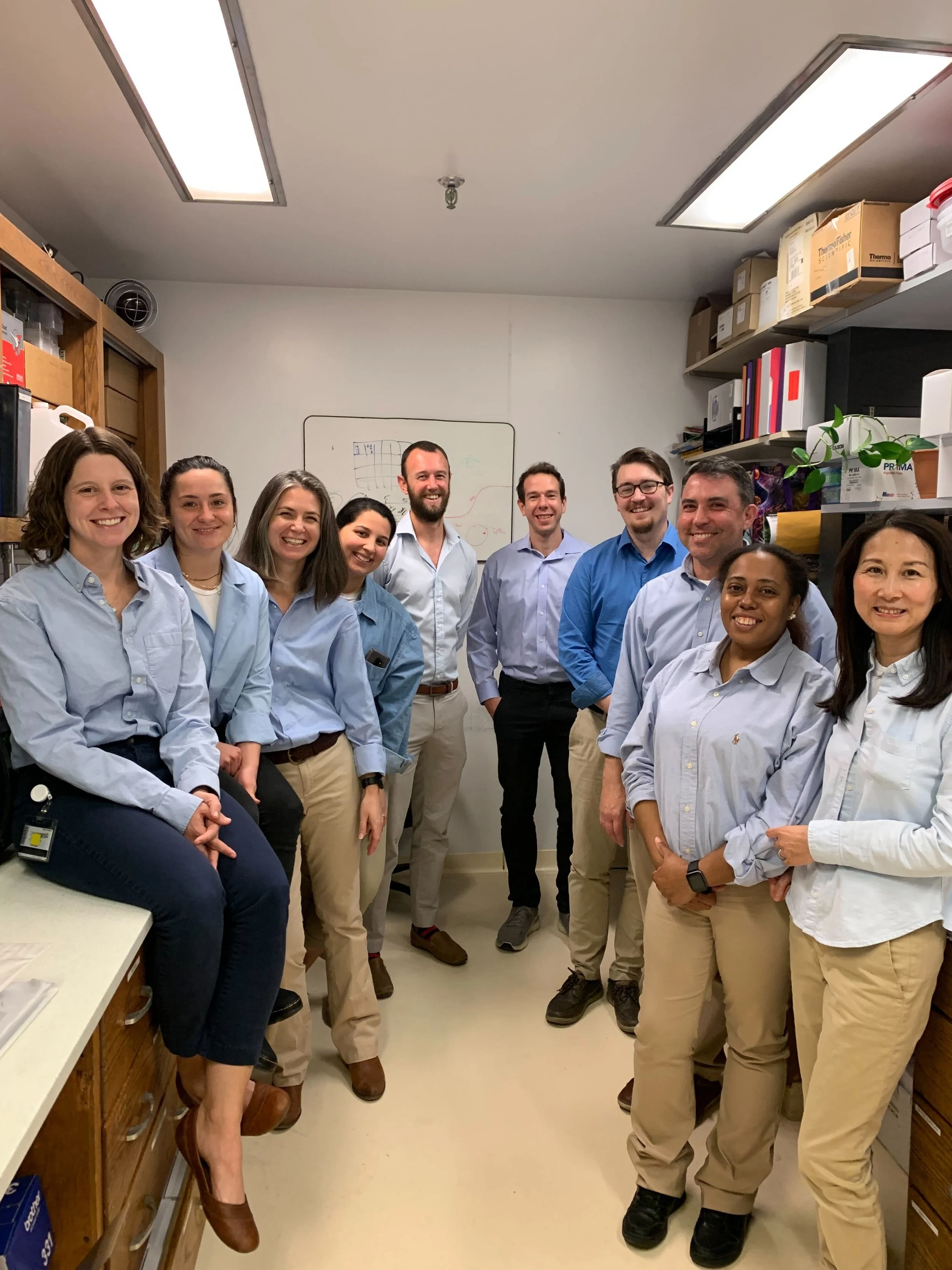 Group of ten people standing together in an office, smiling at the camera.