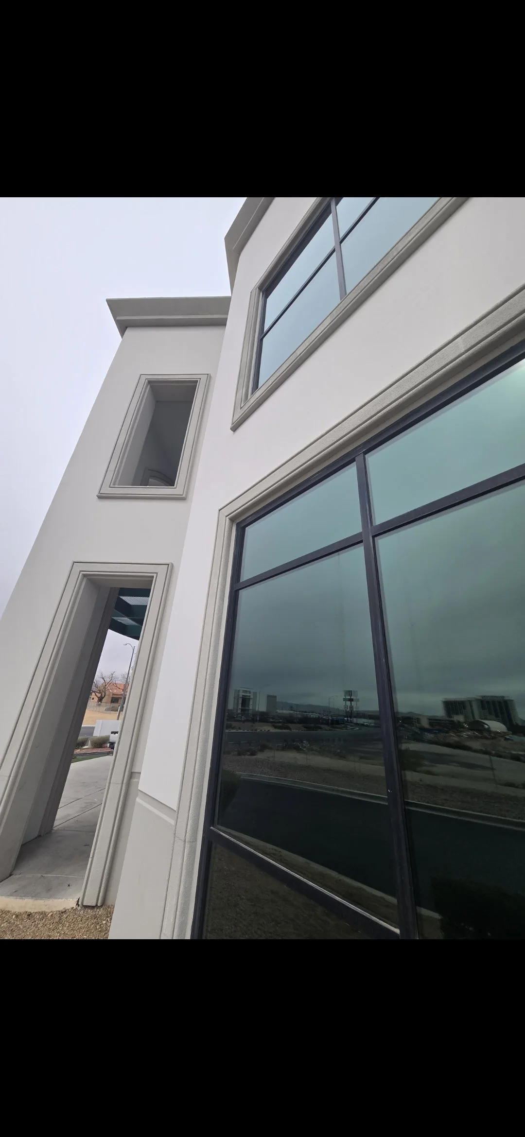 Close-up of a modern building with large tinted windows and white exterior walls, showing multiple window frames properly sealed around the perimeter with Sika caulking.