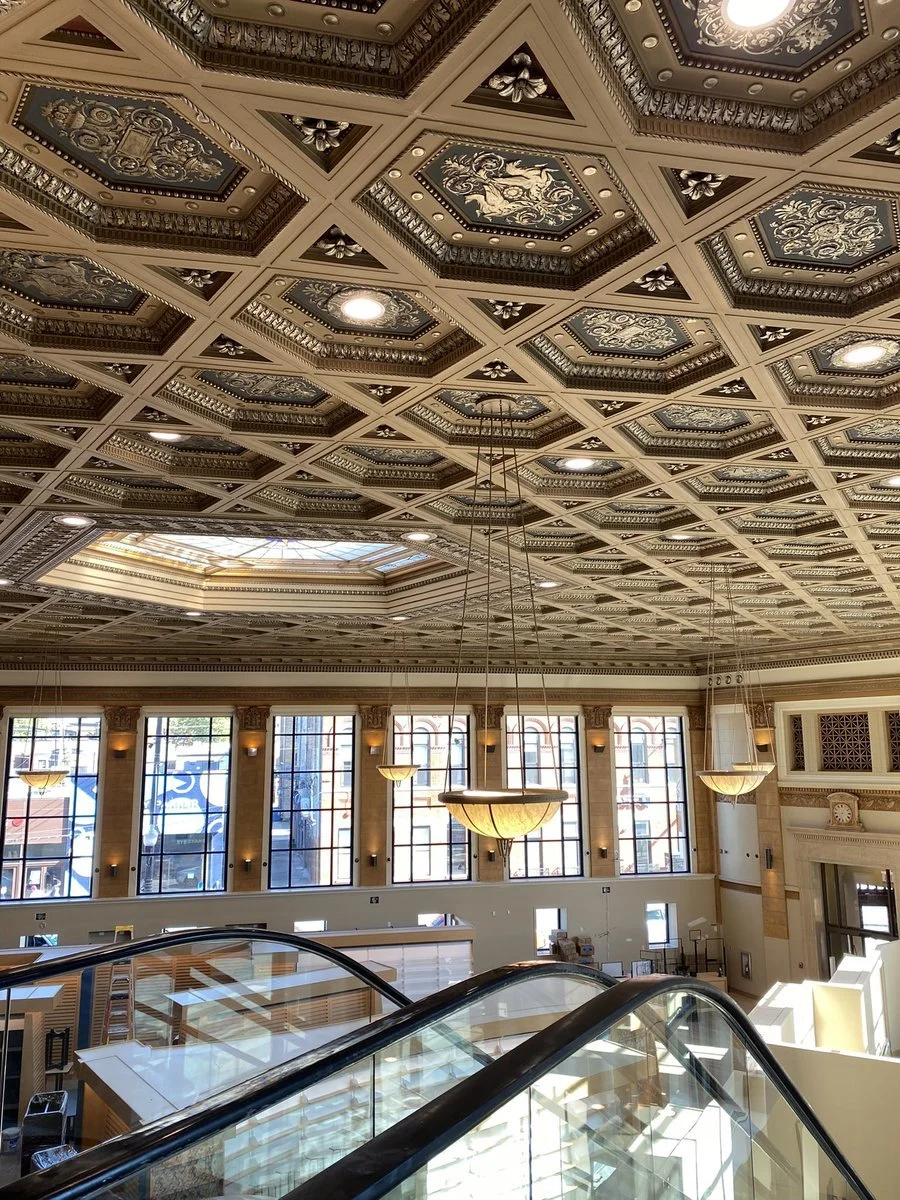 Decorative ornate ceiling with detailed patterns and lighting fixtures in a large building interior.
