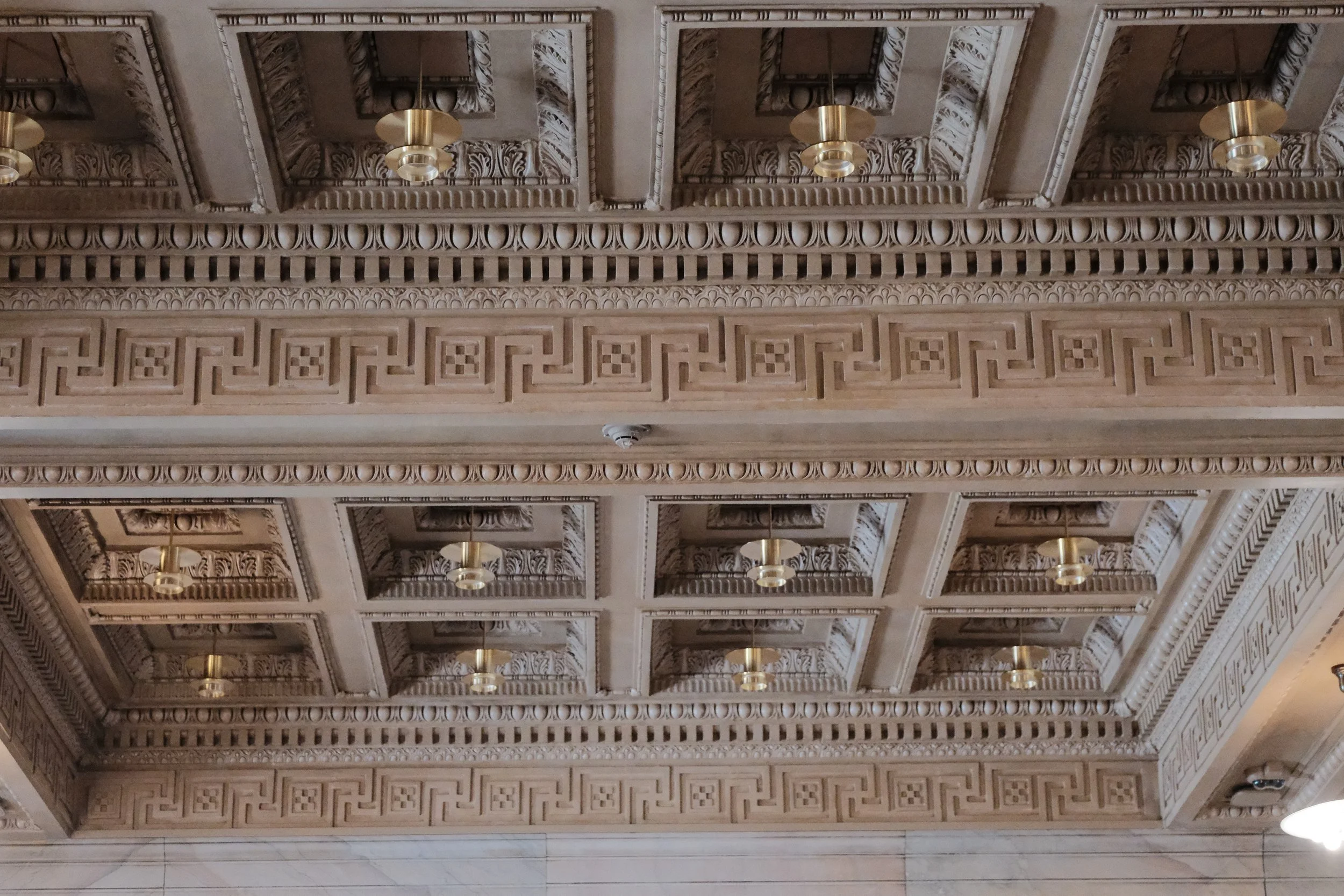 Decorative ceiling with intricate molding, gold light fixtures, and detailed woodwork.