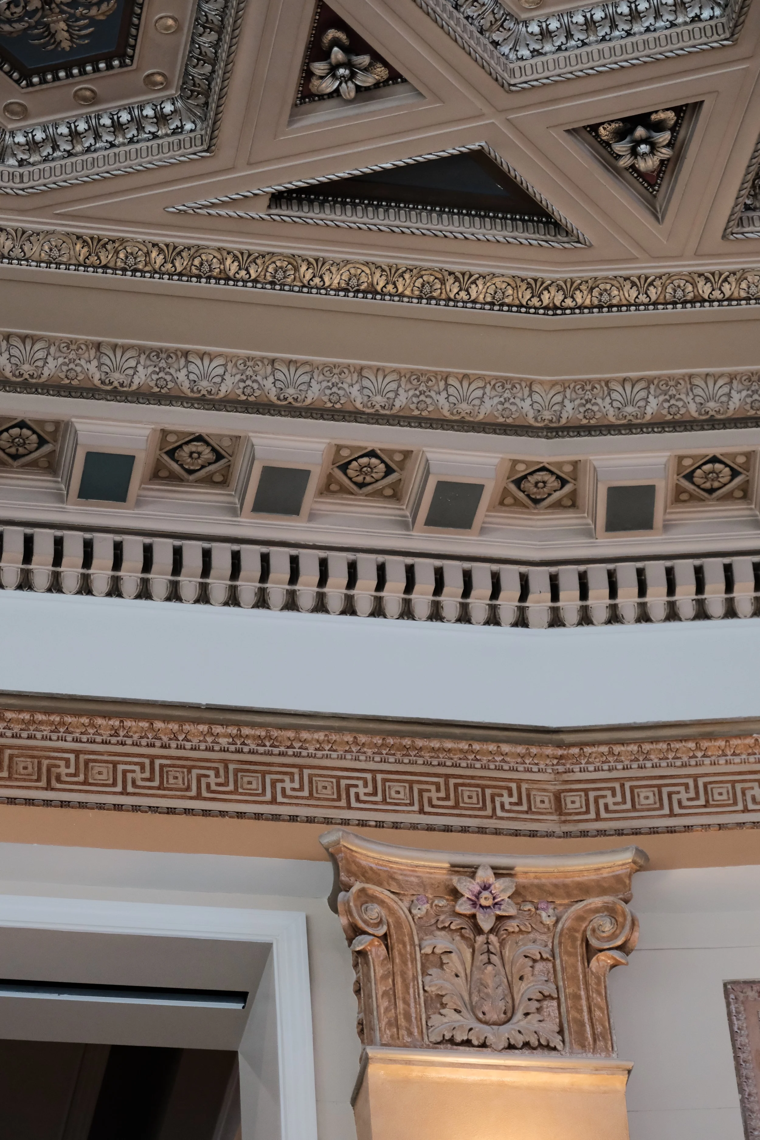 Intricate decorative ceiling with floral and geometric patterns, molding, and an ornamental column with carved floral details.