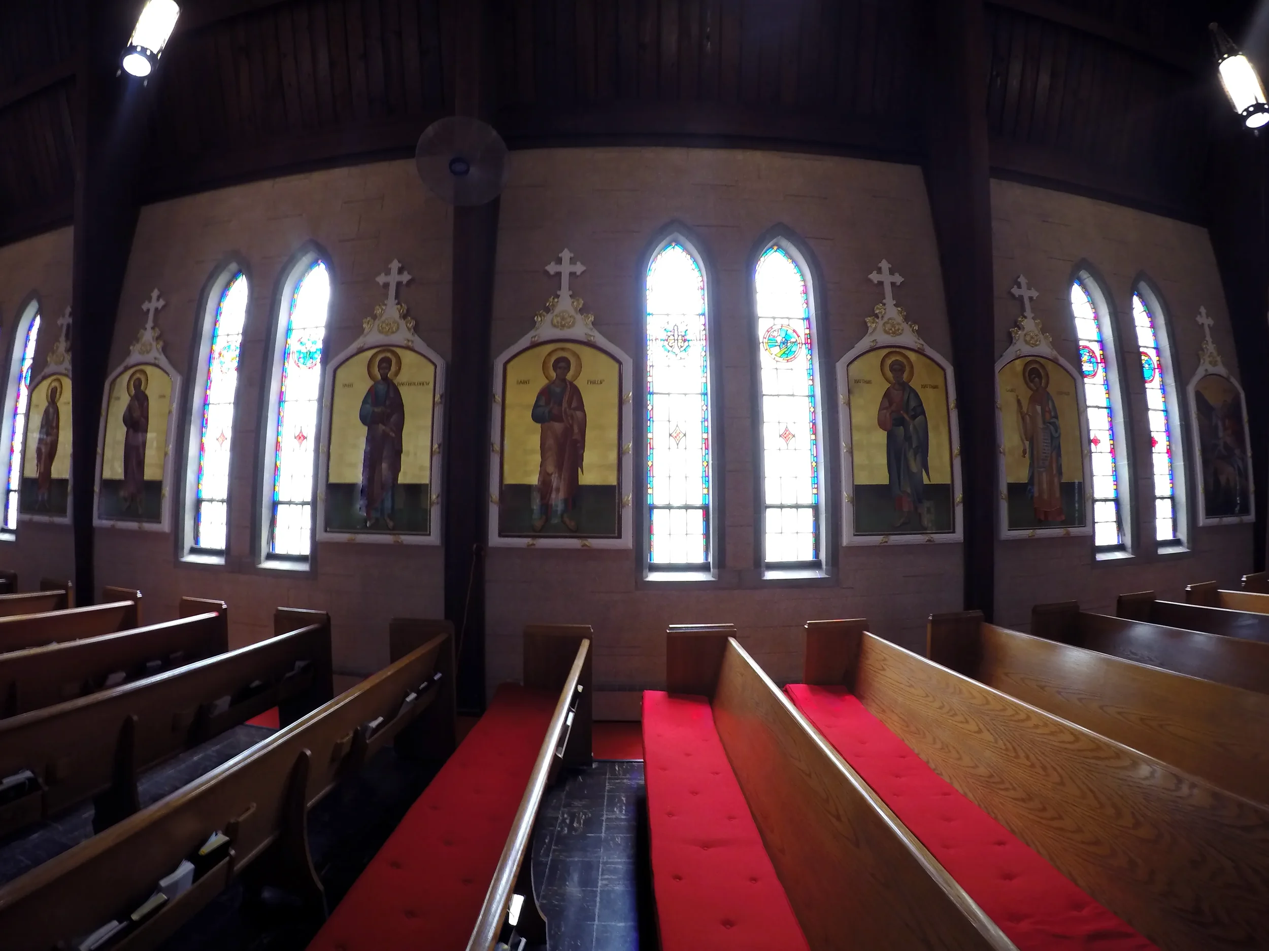 Inside of a church with stained glass windows and religious artwork featuring saints.