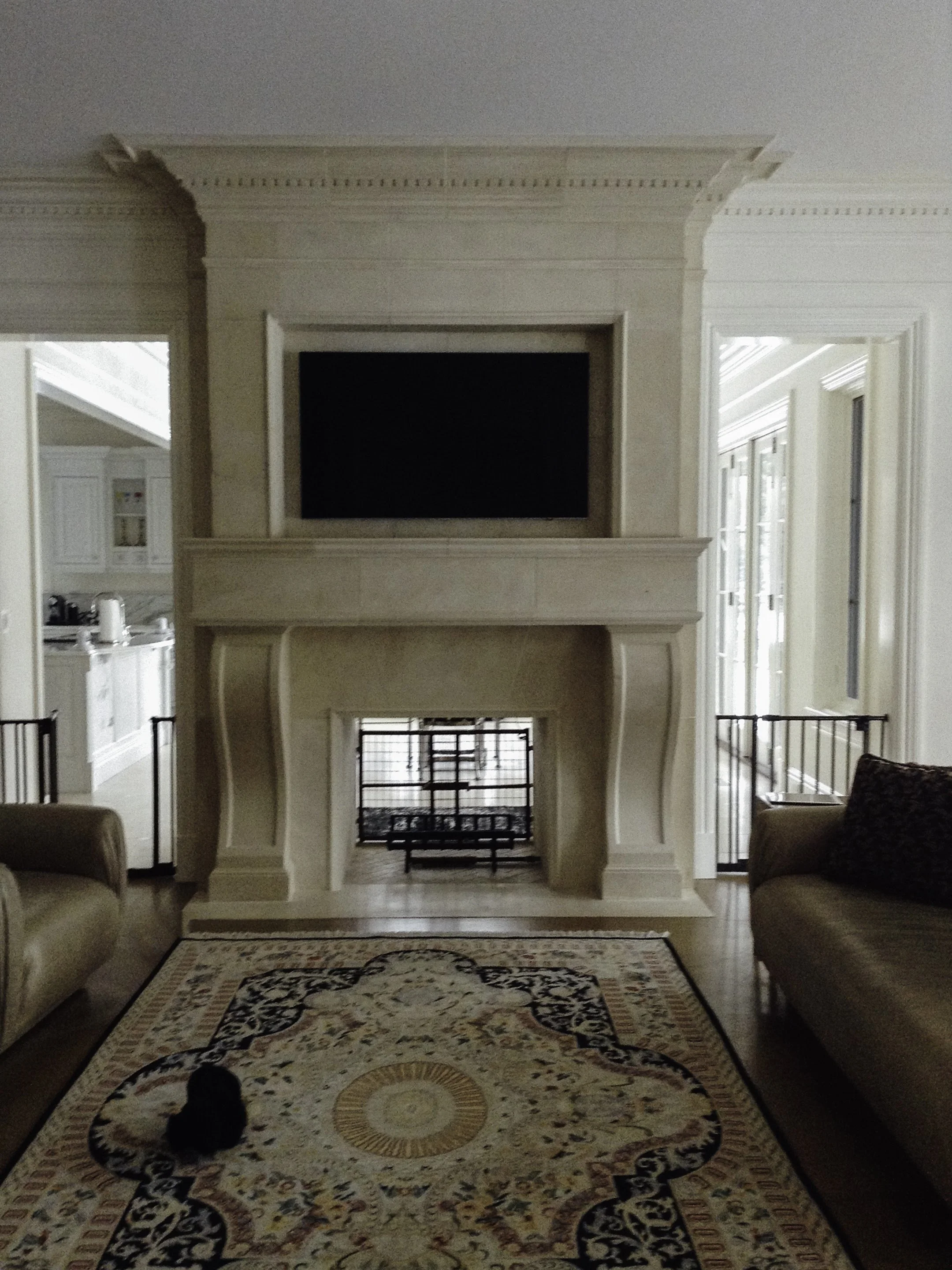 Living room with a fireplace, beige sofas, patterned rug, and TV above the fireplace.