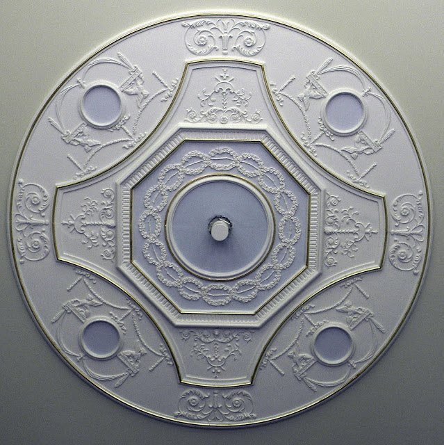 Ornate ceiling medallion with floral and scroll designs, featuring a central circular motif and four smaller circles around it.