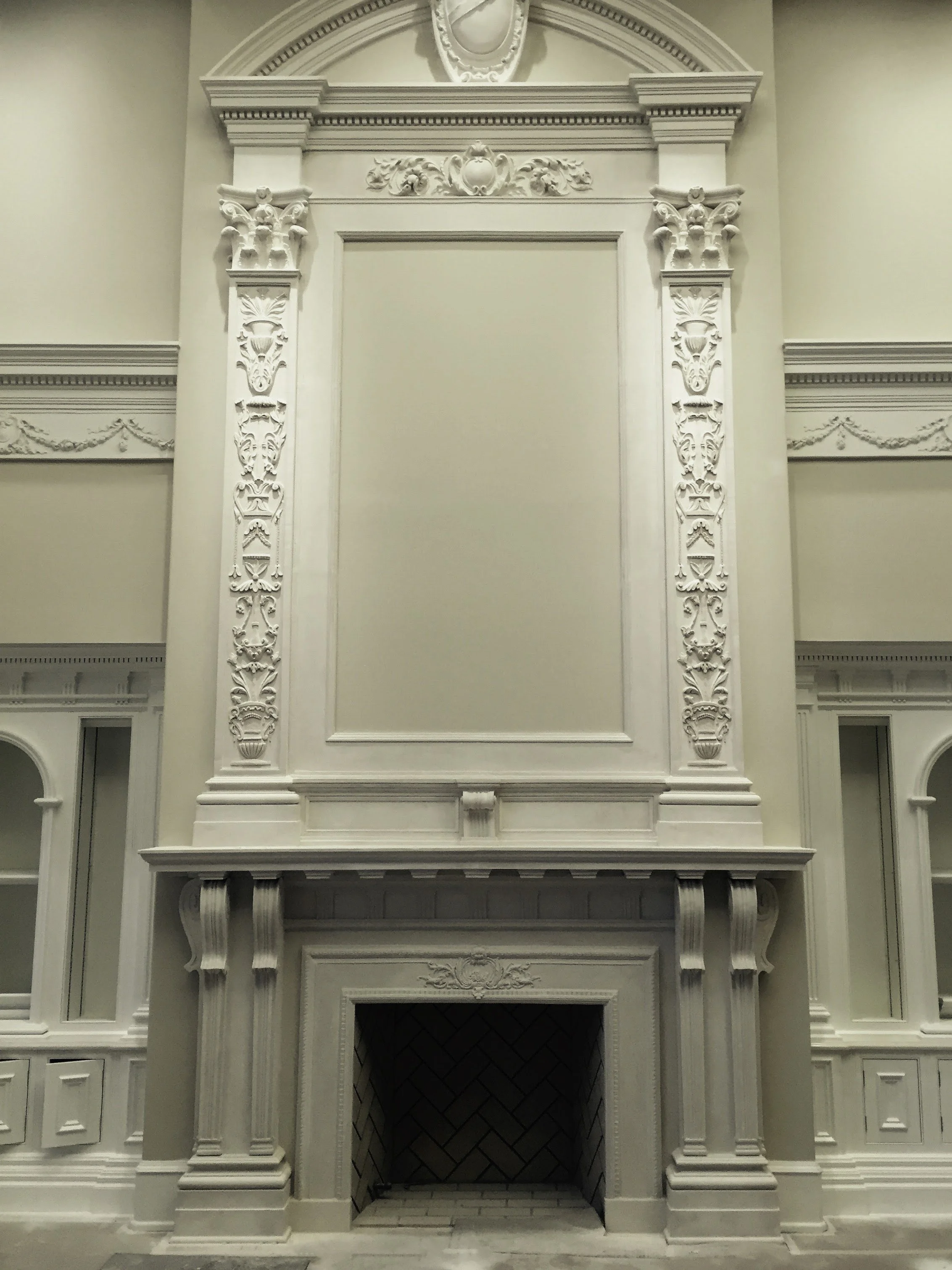 Ornate white fireplace with detailed molding and decorative trim, set within a wall with similar decorative elements.