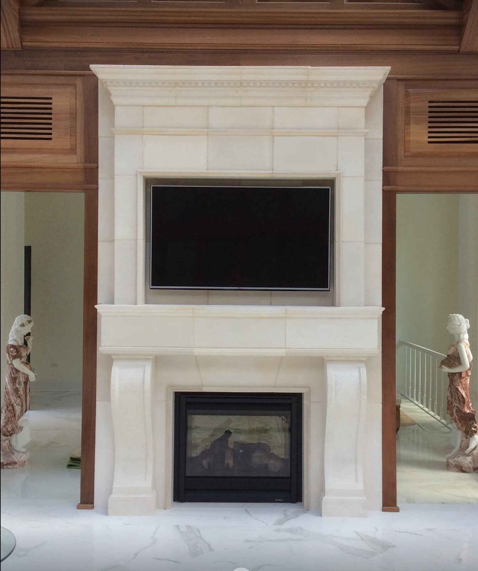 A living room with a white stone fireplace and a flat-screen TV mounted above it.