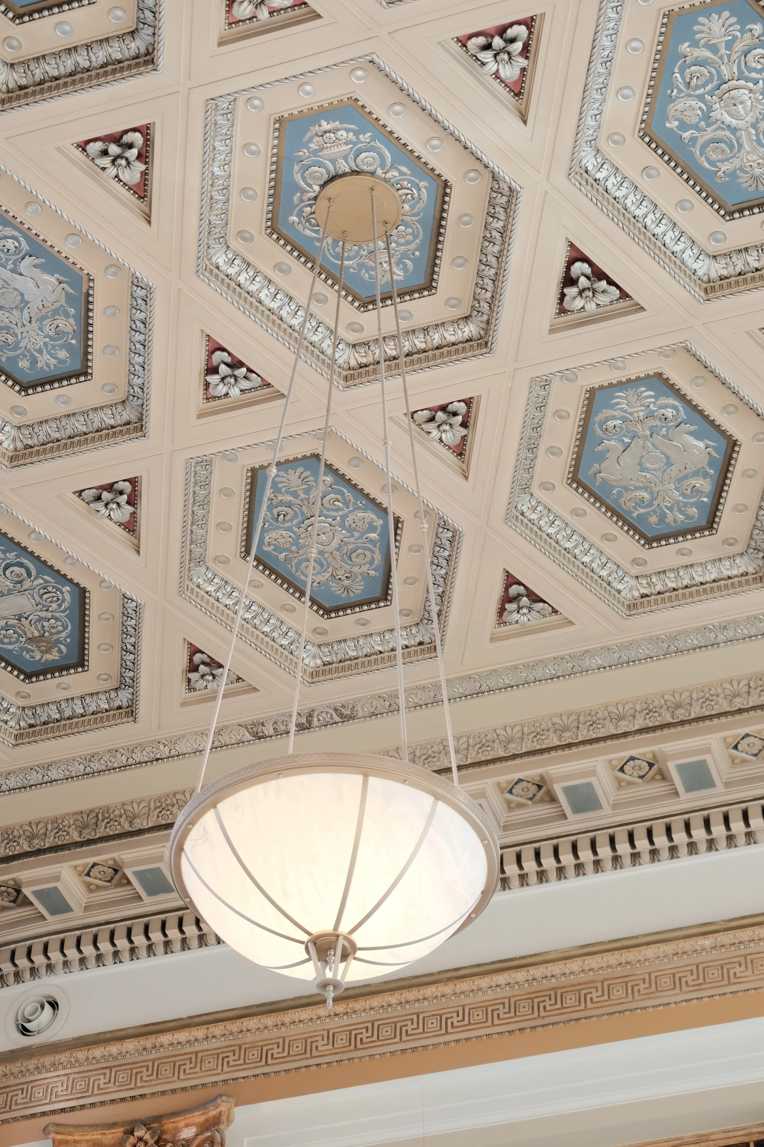 Ornate ceiling with decorative floral patterns and a hanging light fixture.
