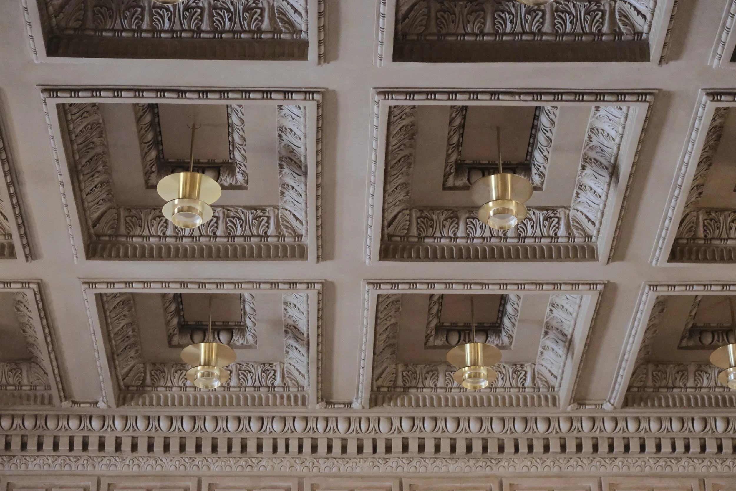 Decorative ceiling with ornate molding and four hanging gold and white light fixtures.