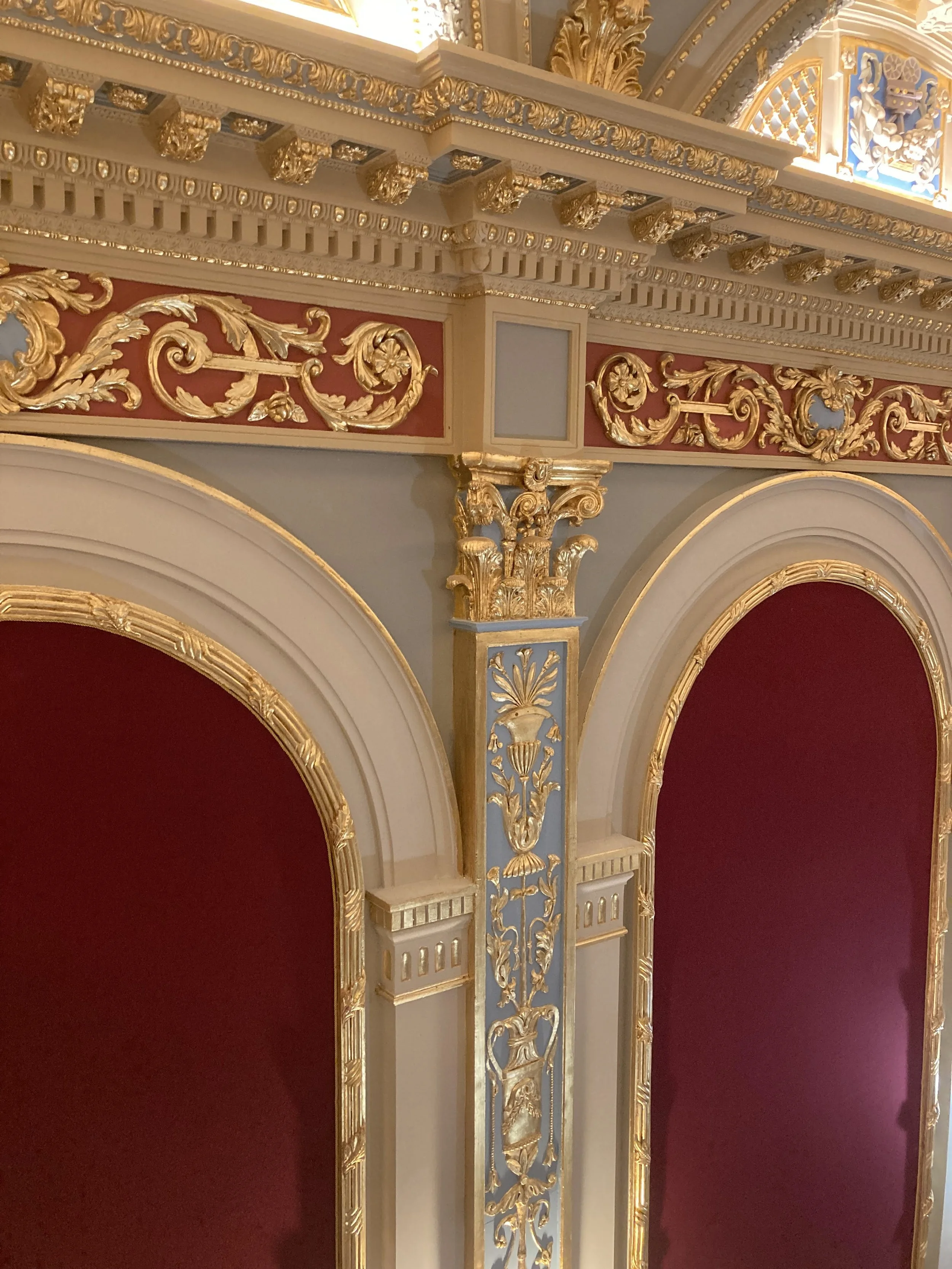 Elegant theater box with ornate gold detailing, cream-colored trim, and rich red velvet curtains.