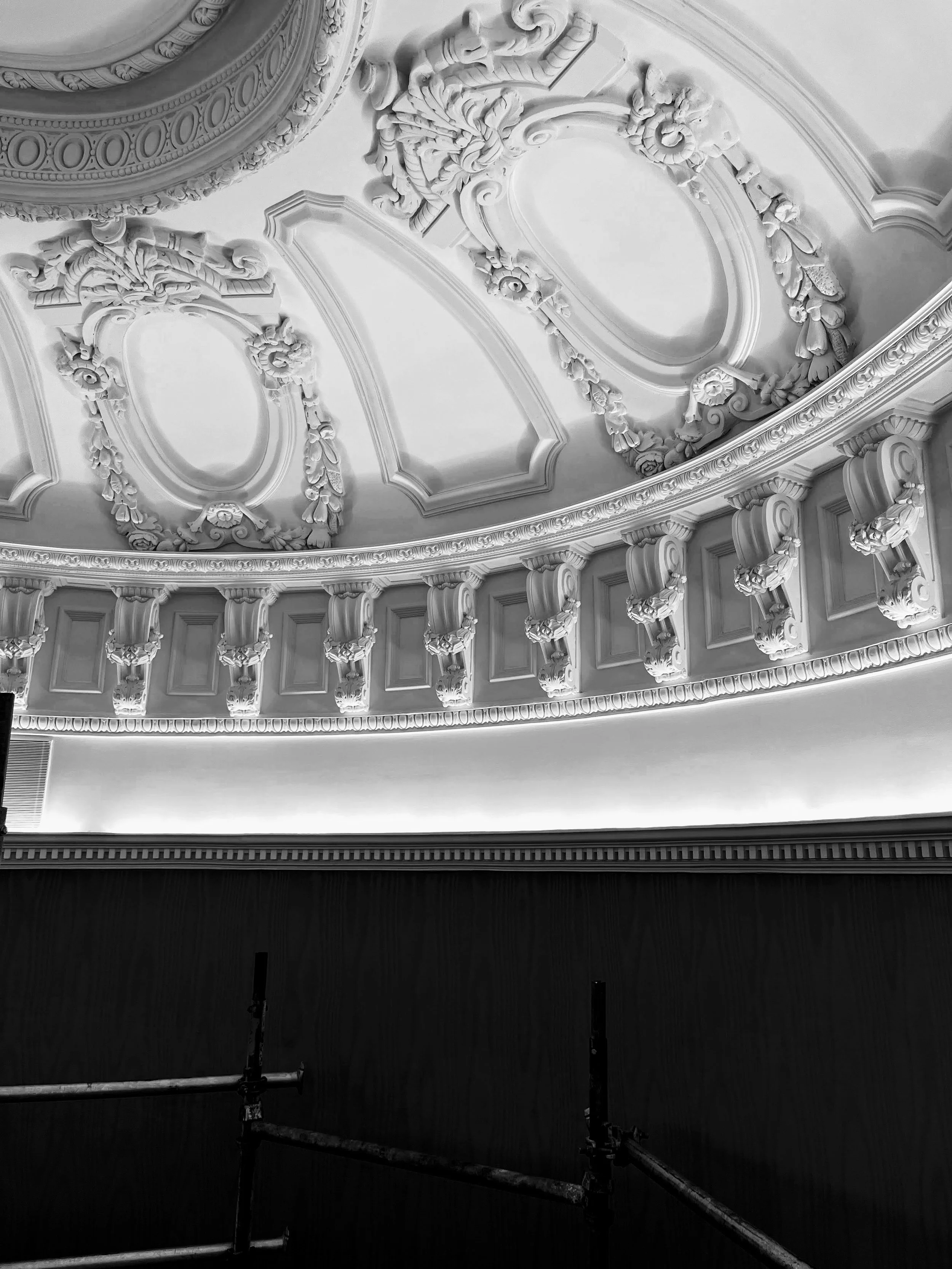Ornate ceiling with decorative moldings and architectural details in a historic building, black and white photo.