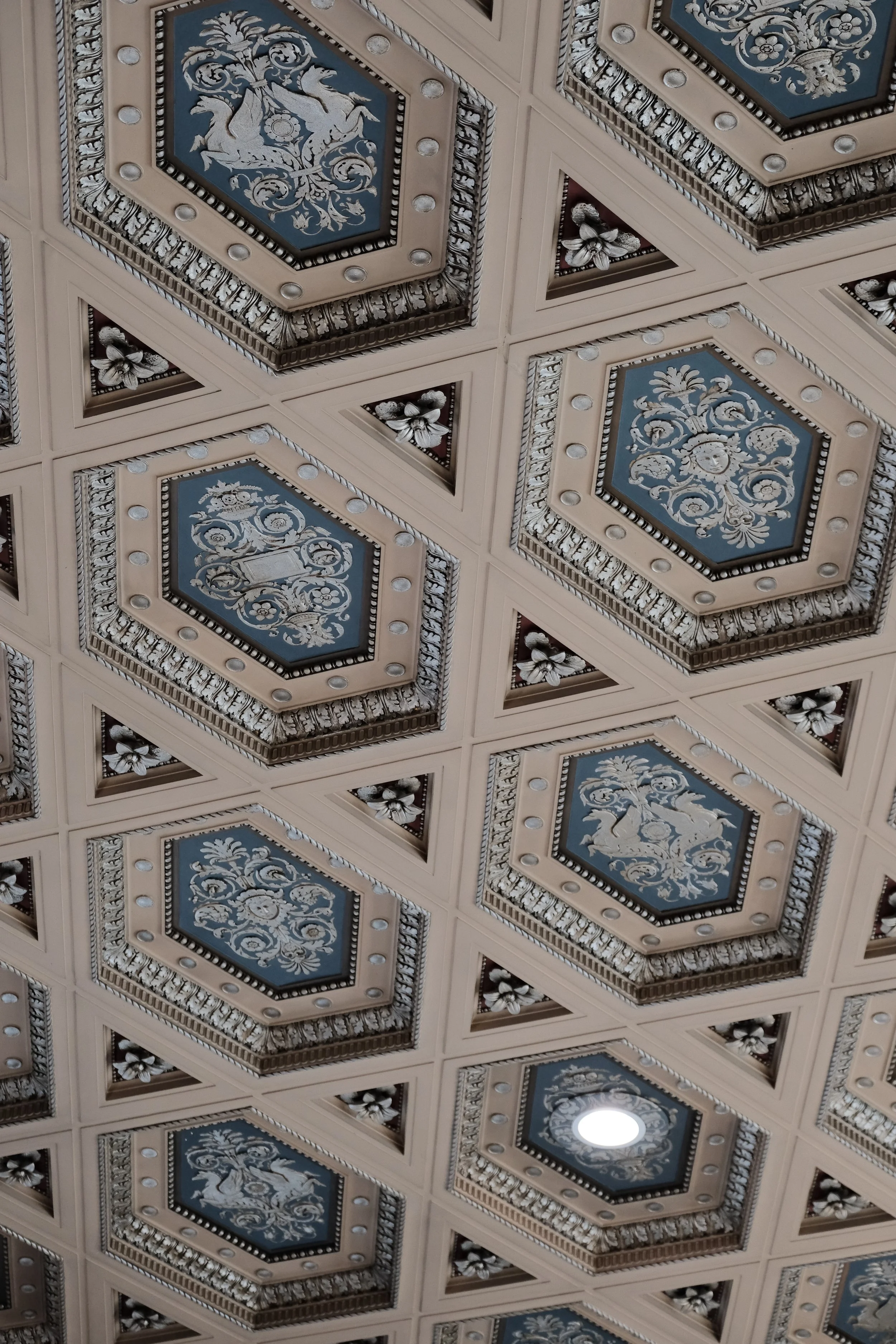Ceiling with ornate, patterned, hexagonal tiles featuring floral and mythological figures design in shades of bue, beige, and white.