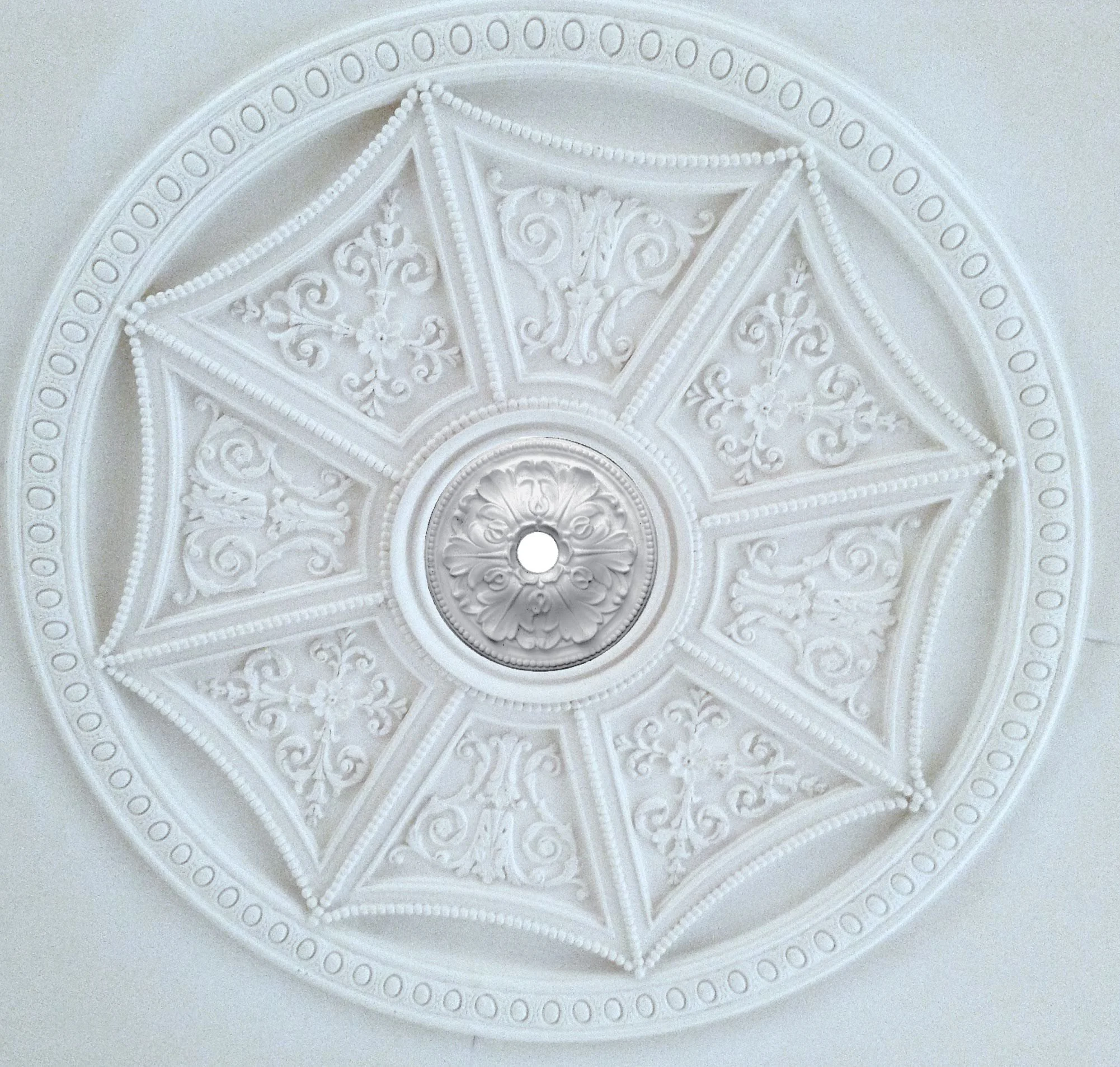 Ornate white ceiling medallion with detailed floral and scroll patterns surrounding a central hole.