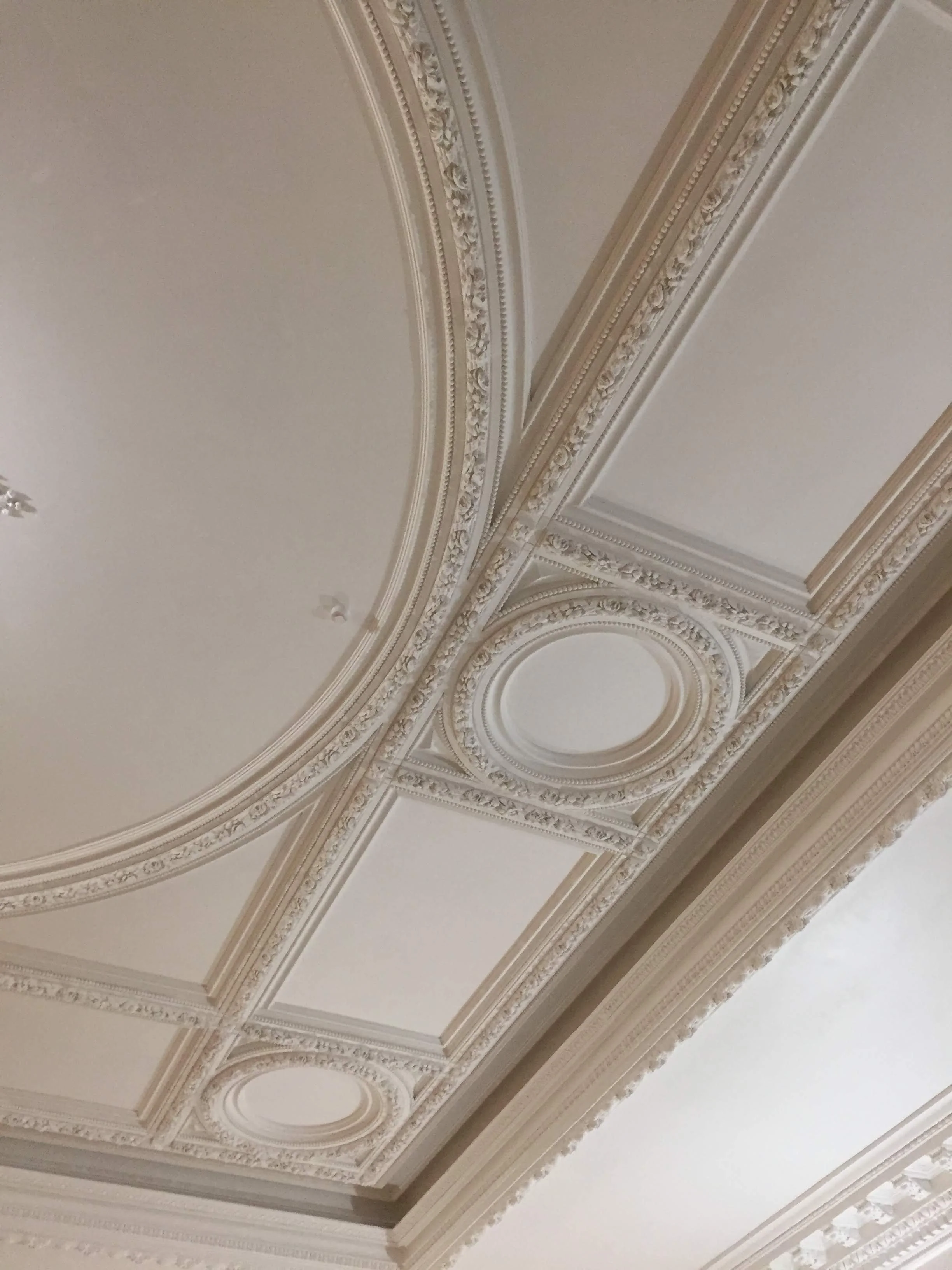 Decorative ceiling with ornate molding, circular and rectangular panels, and intricate trim in a classical style.