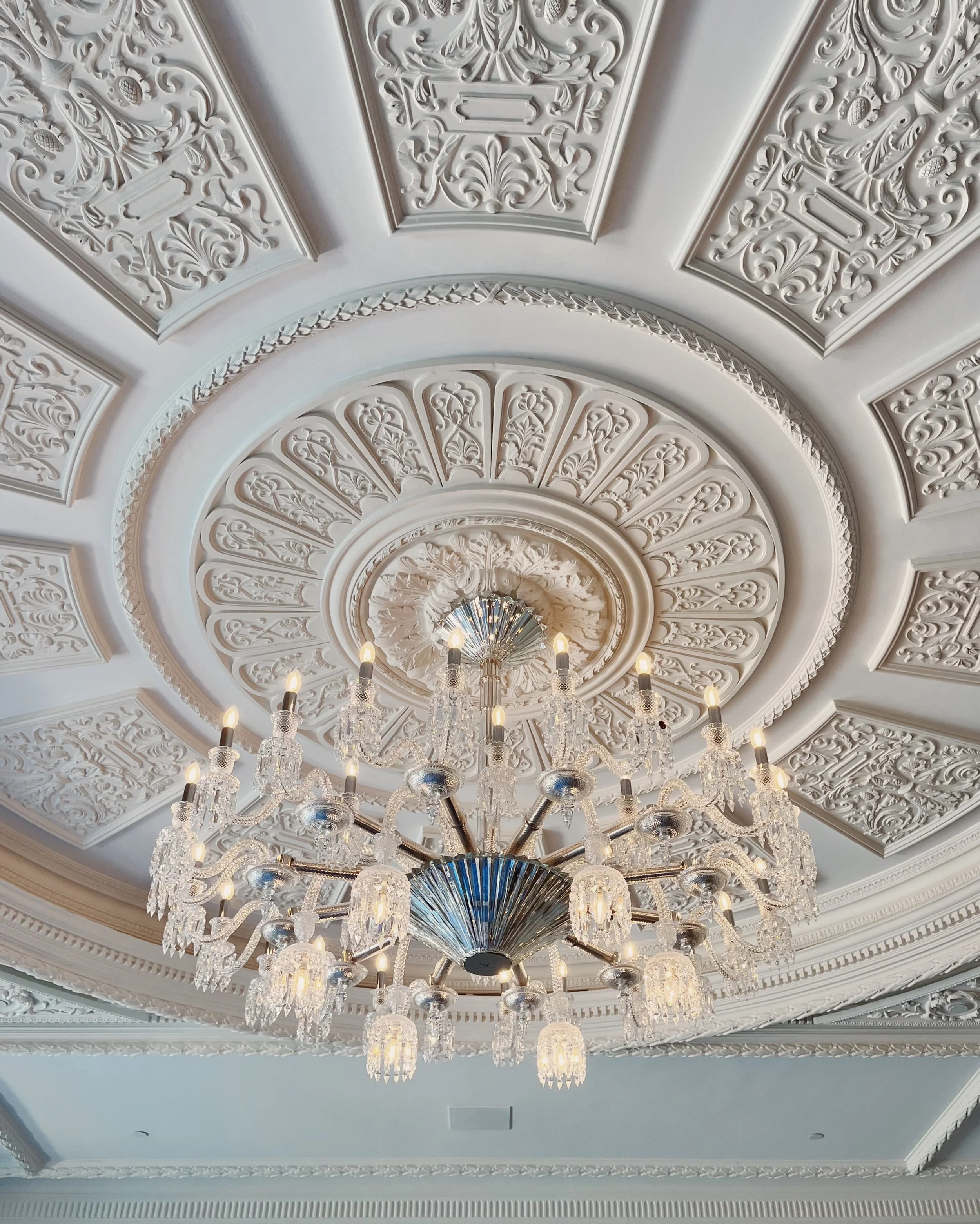 Ornate white ceiling with intricate molding and a large crystal chandelier.