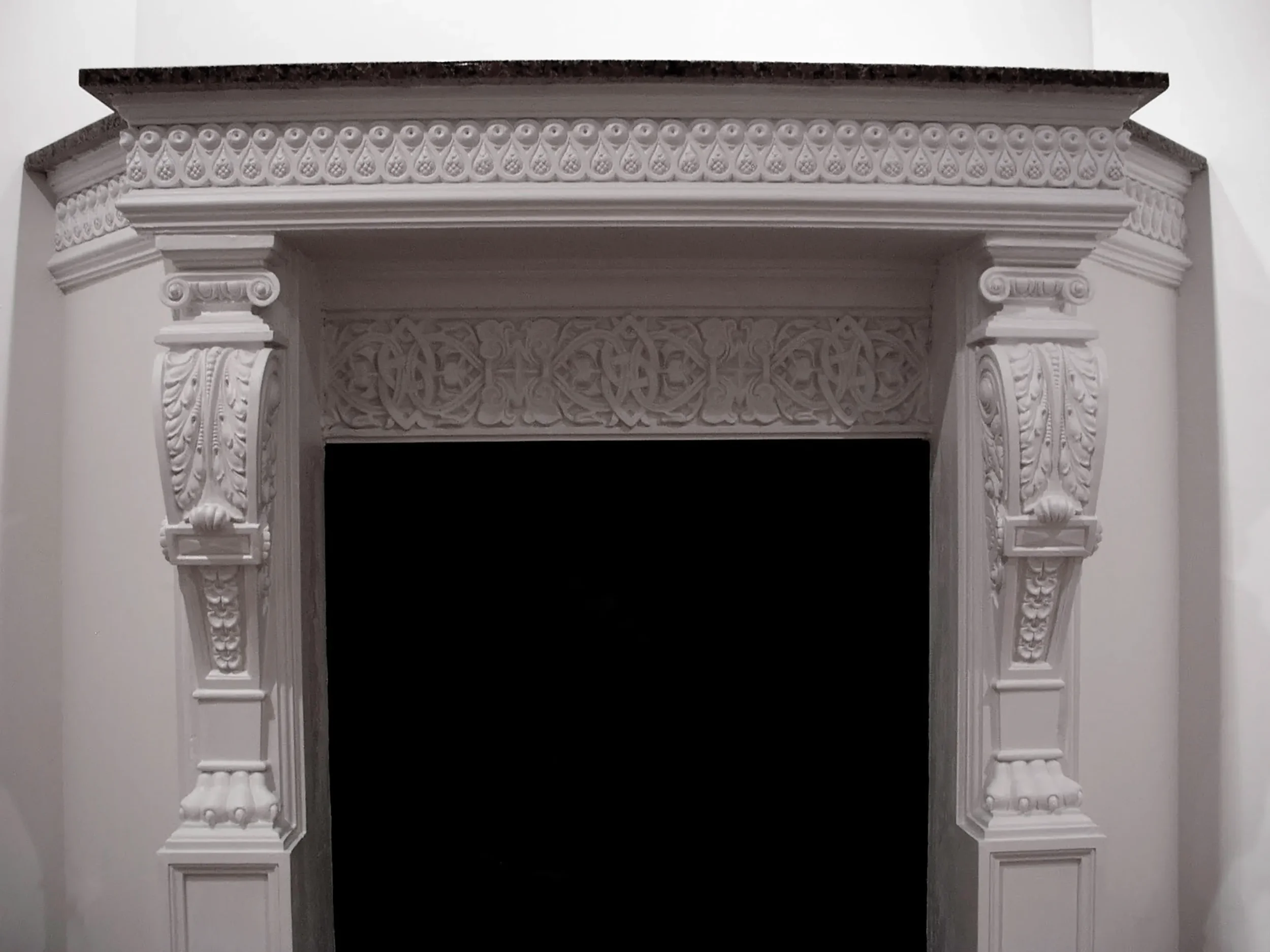 Ornate white fireplace mantel with detailed carvings and a dark marble top.