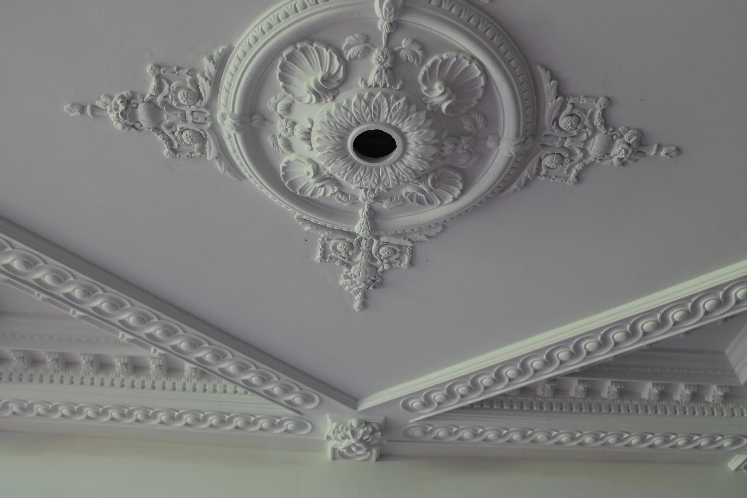 Ornate ceiling medallion with intricate molding details, decorative patterns, and a central hole for a light fixture.