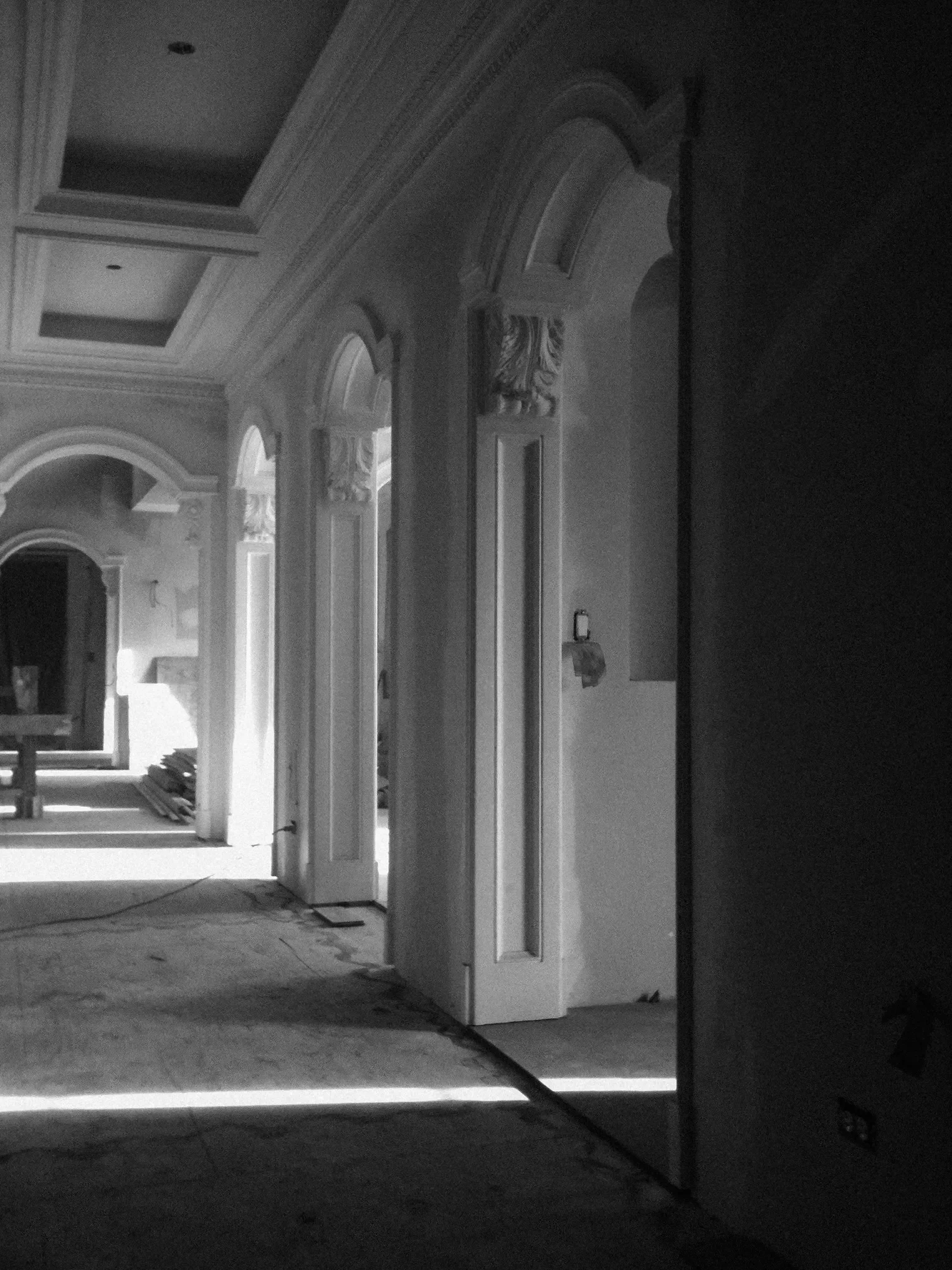 Black and white photo of interior hallway of a house under construction, with ornate architectural details and partially finished flooring.