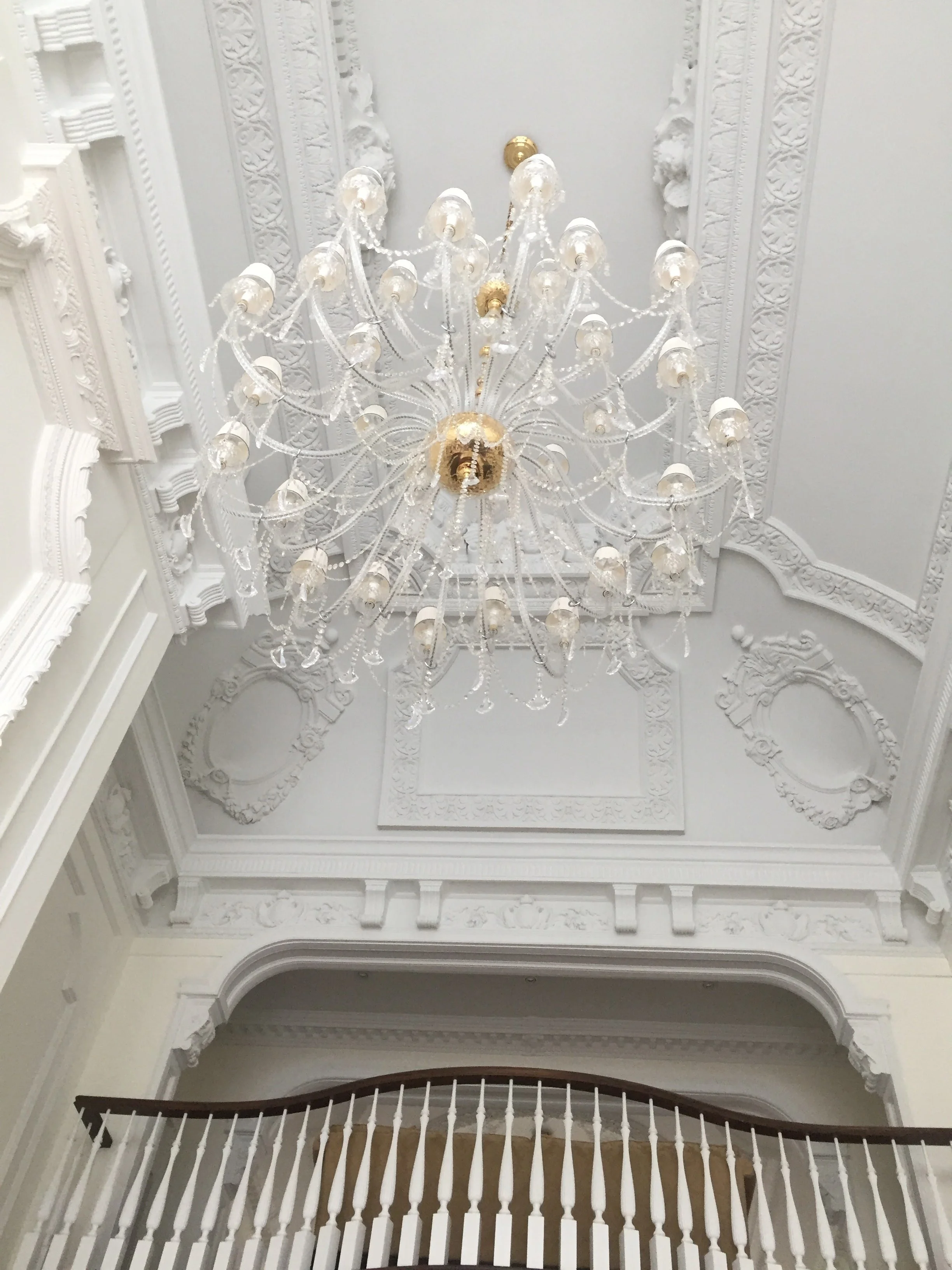 Elegant white ceiling with ornate plaster molding and a large crystal chandelier hanging in the center.