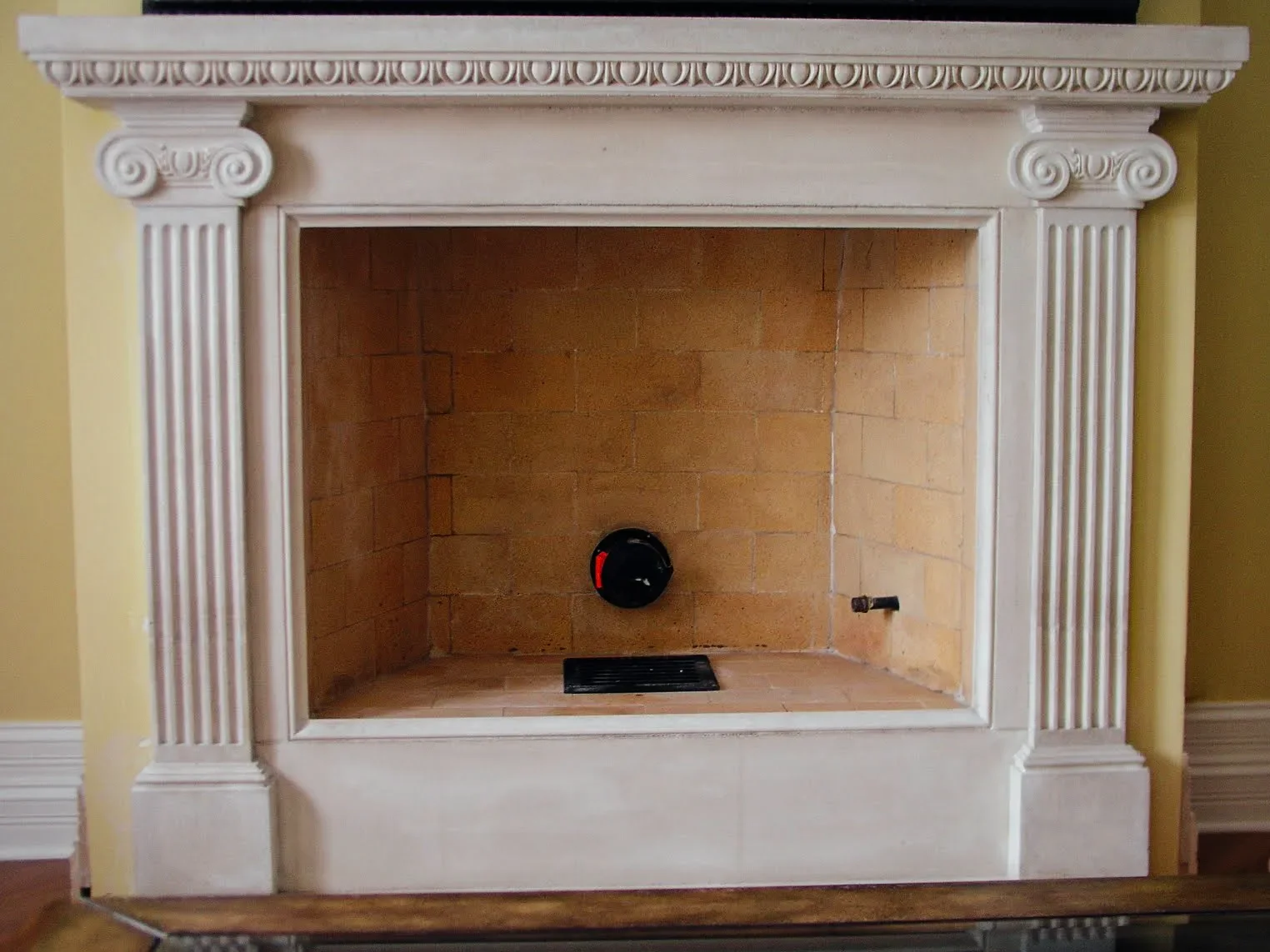 Empty decorative fireplace with beige brick interior, cream-colored mantel, and Corinthian-style columns on sides.