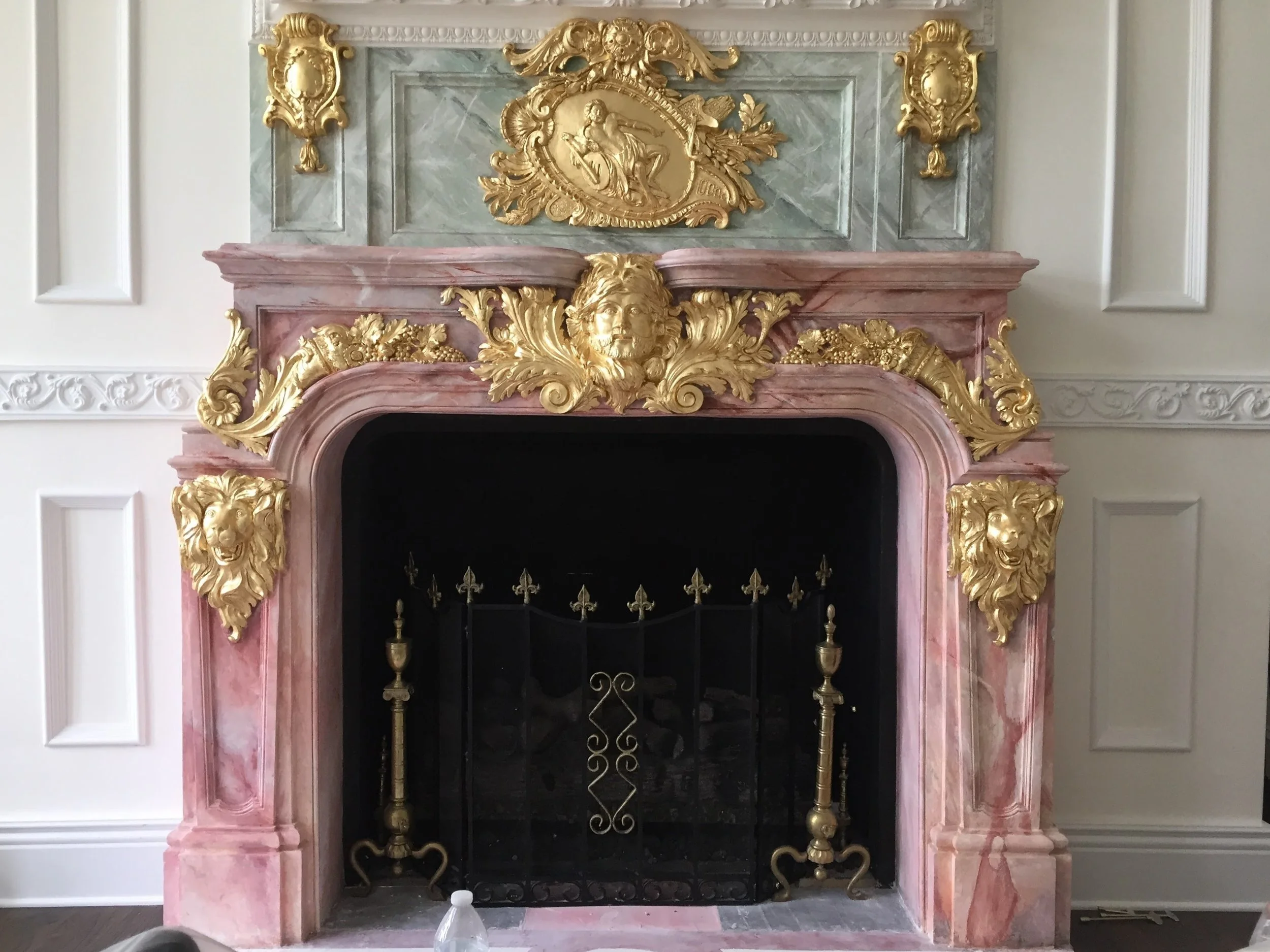 Decorative fireplace with pink and gold marble and ornate gold accents, including lion and human face carvings.