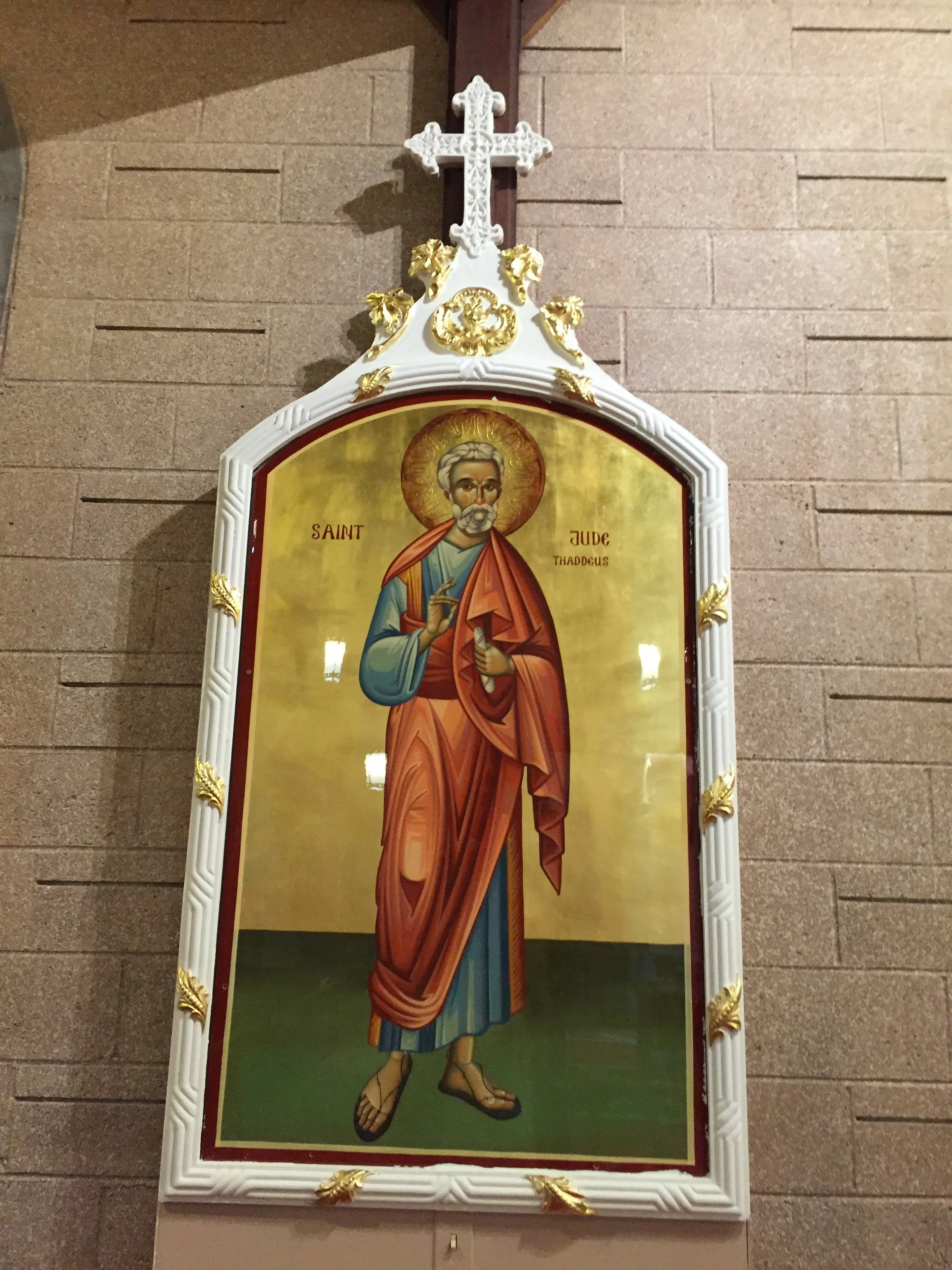 Religious icon of Saint Jude Thaddeus depicted as a bearded man with a halo, wearing traditional robes, holding a small image of Jesus Christ, and the gesture of blessing with his right hand. The icon is framed within a decorative white frame with go