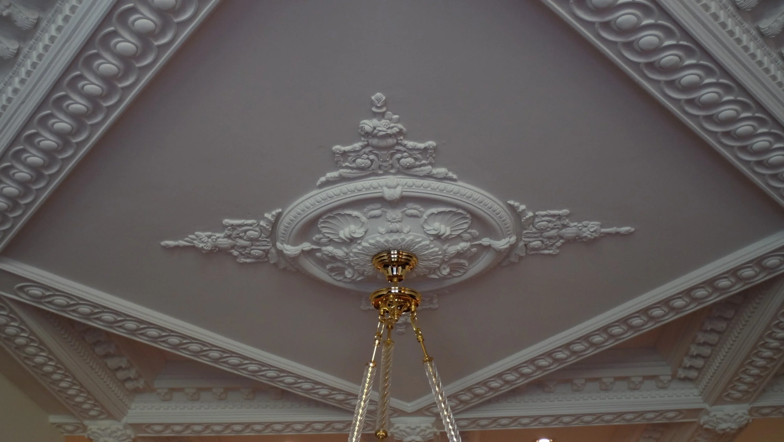 Decorative ceiling with intricate plaster molding and a gold chandelier hanging in the center.