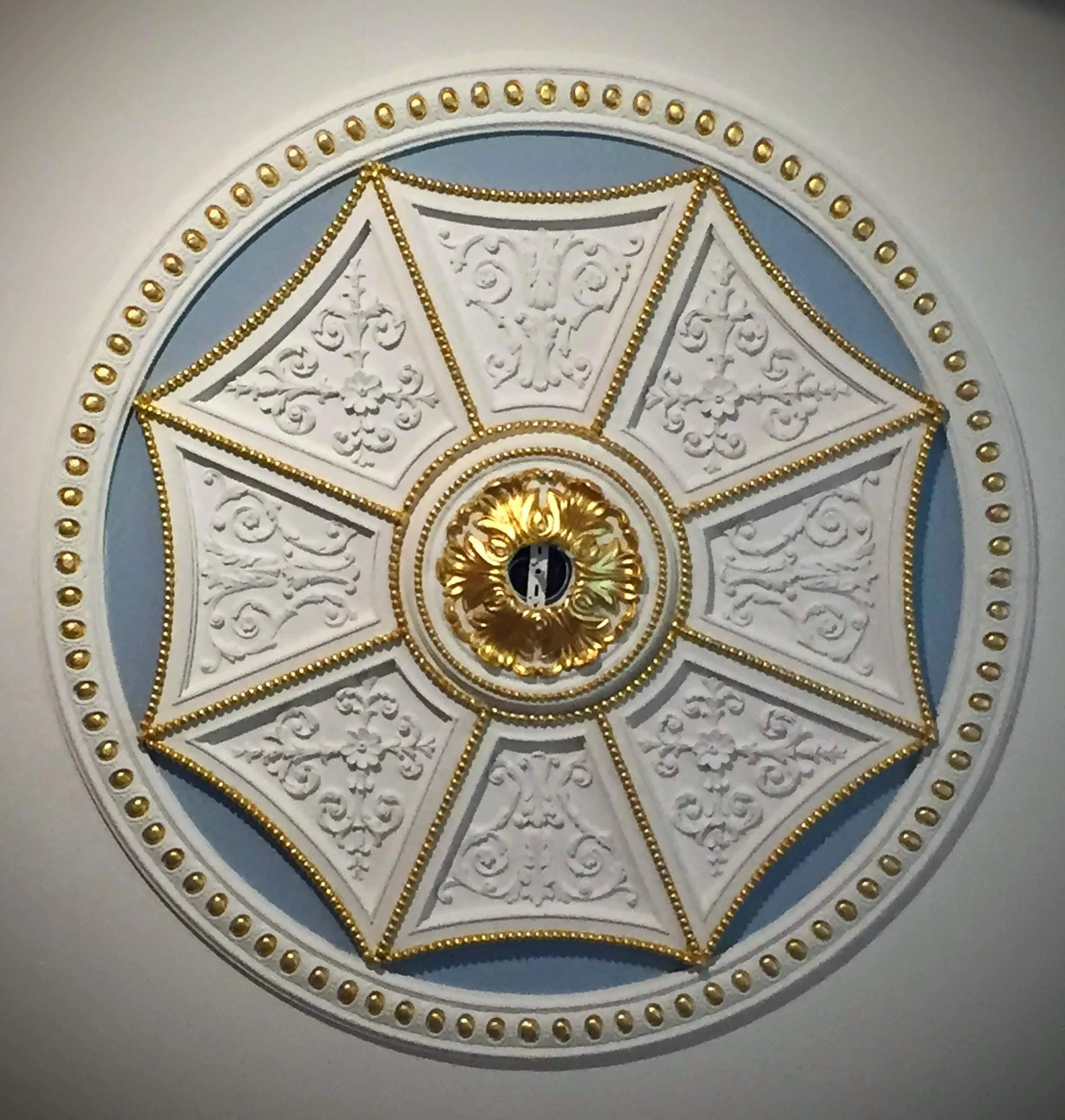 Ornate ceiling medallion with gold accents and intricate white plaster design, featuring a central gold ornament around a light fixture