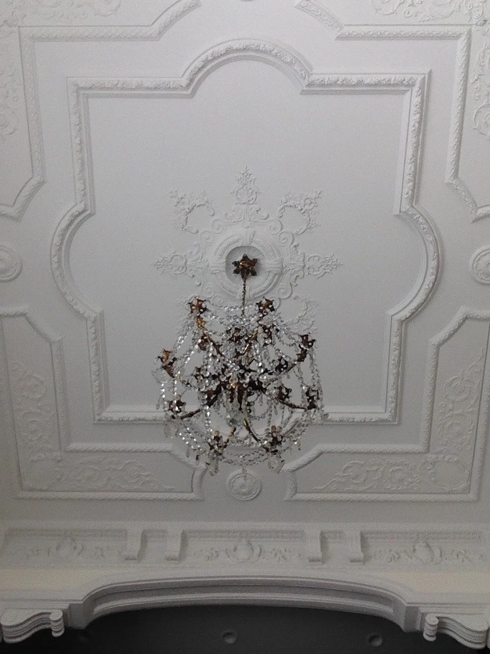 Ornate white ceiling with decorative molding and a large chandelier hanging in the center.