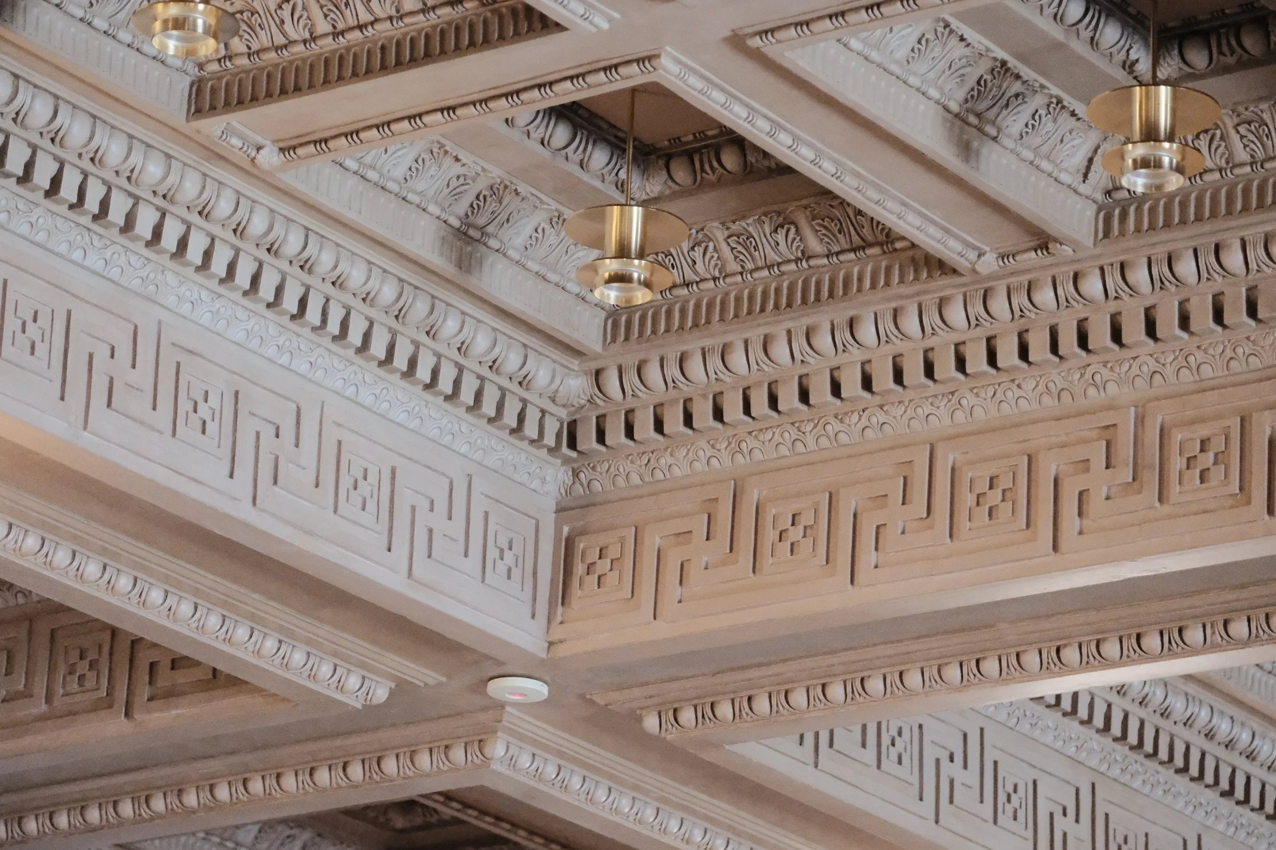 Intricate wooden ceiling with detailed molding, geometric patterns, and modern hanging light fixtures.