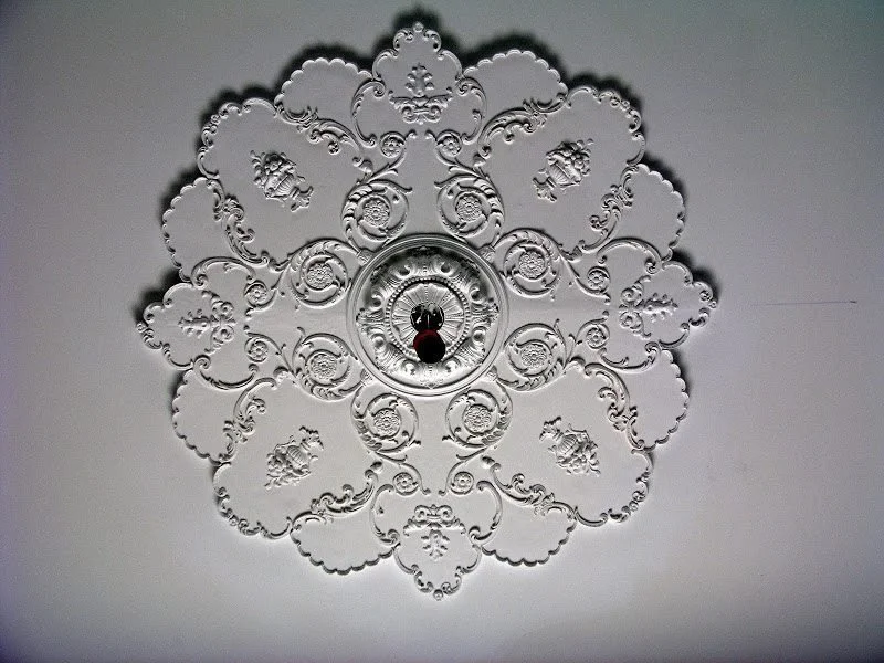 A decorative ceiling with ornate silver pattern and an antique-style light fixture in the center, resembling a chandelier or ceiling medallion.