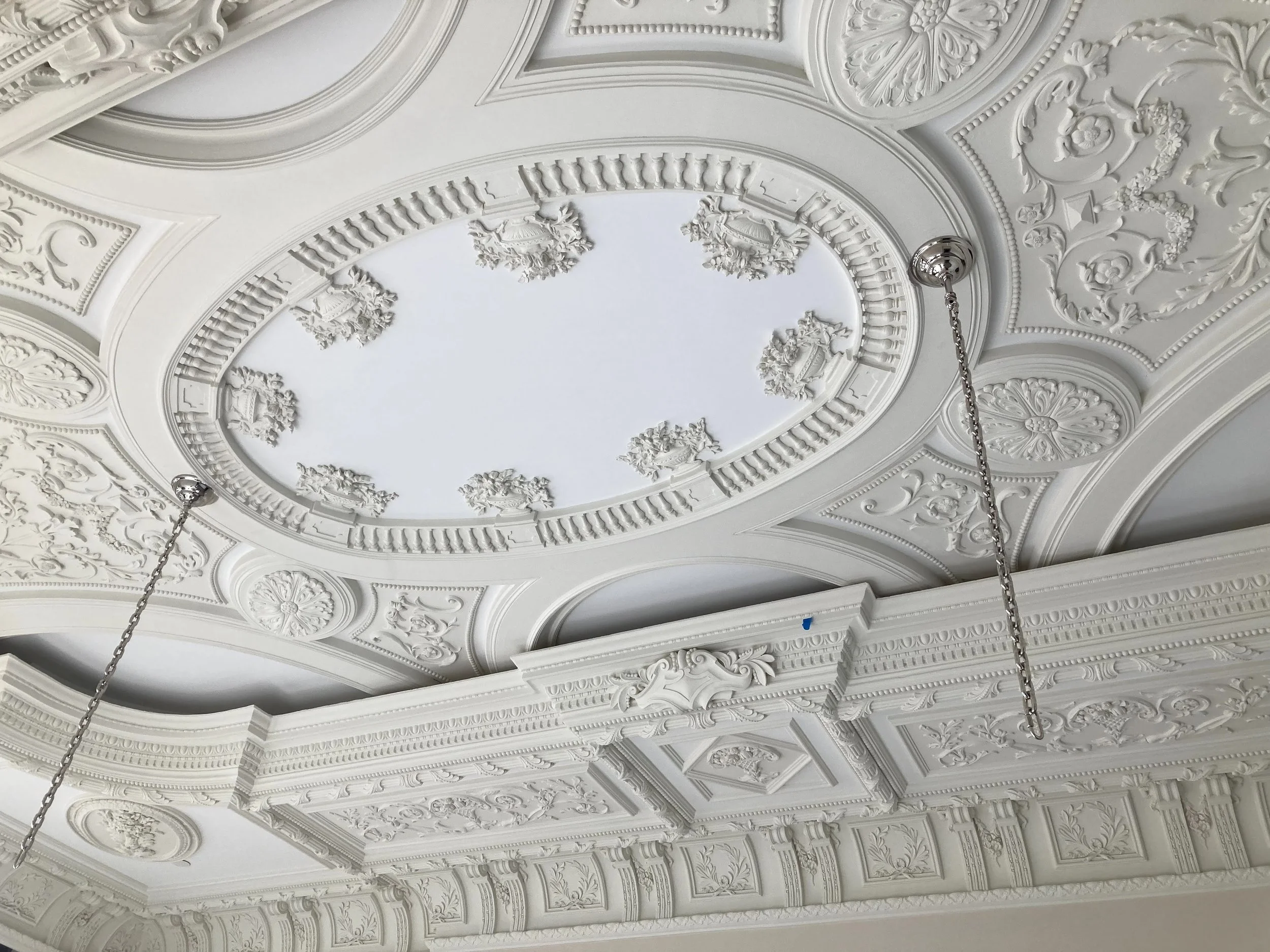 Ornate white ceiling with detailed moldings, decorative plasterwork, and hanging chains.