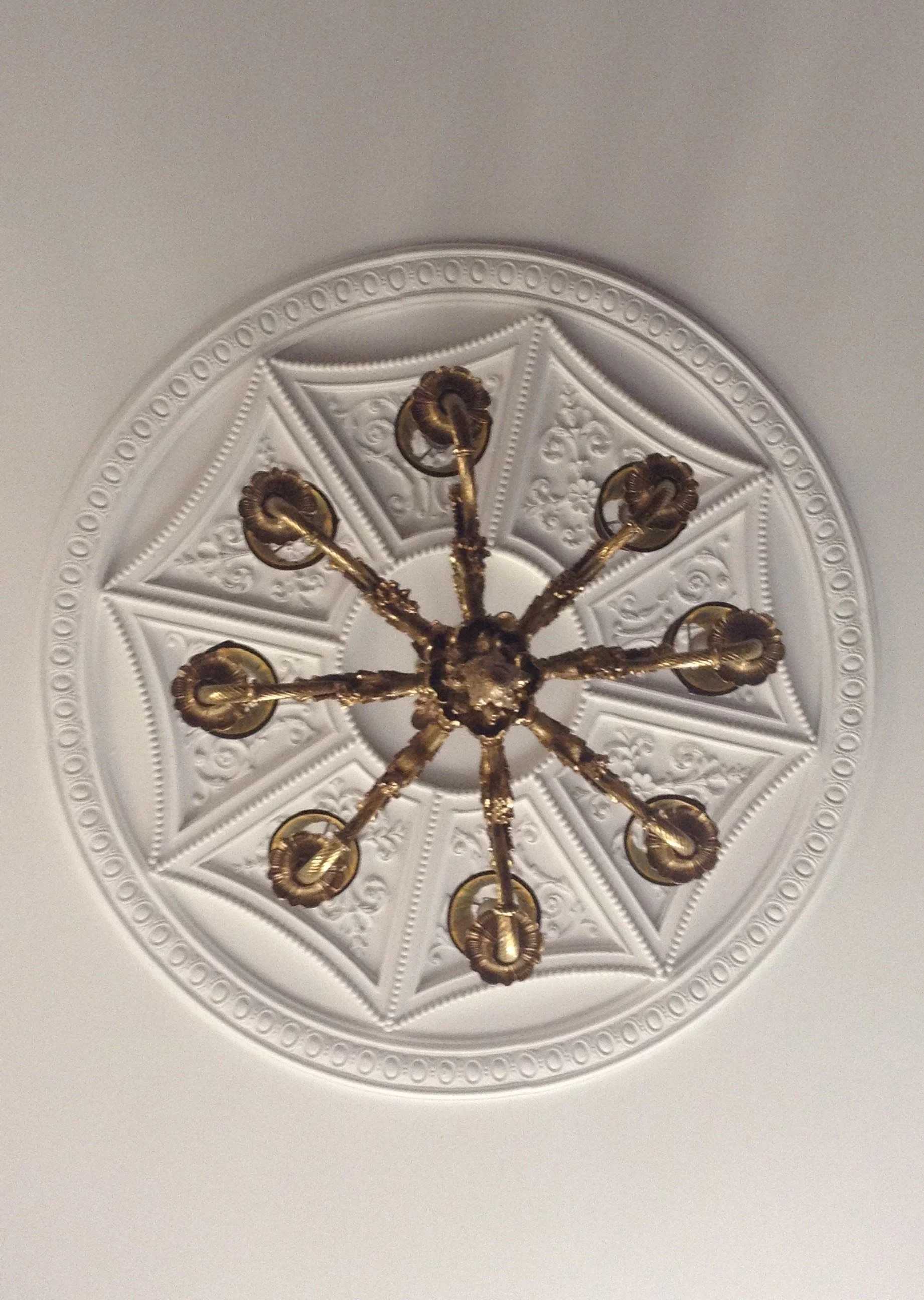 Ornate ceiling medallion with a brass chandelier hanging from the center, featuring multiple candle-like lights.
