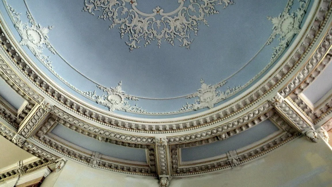 An ornate, decorative ceiling with intricate molding and embellishments in pastel colors.