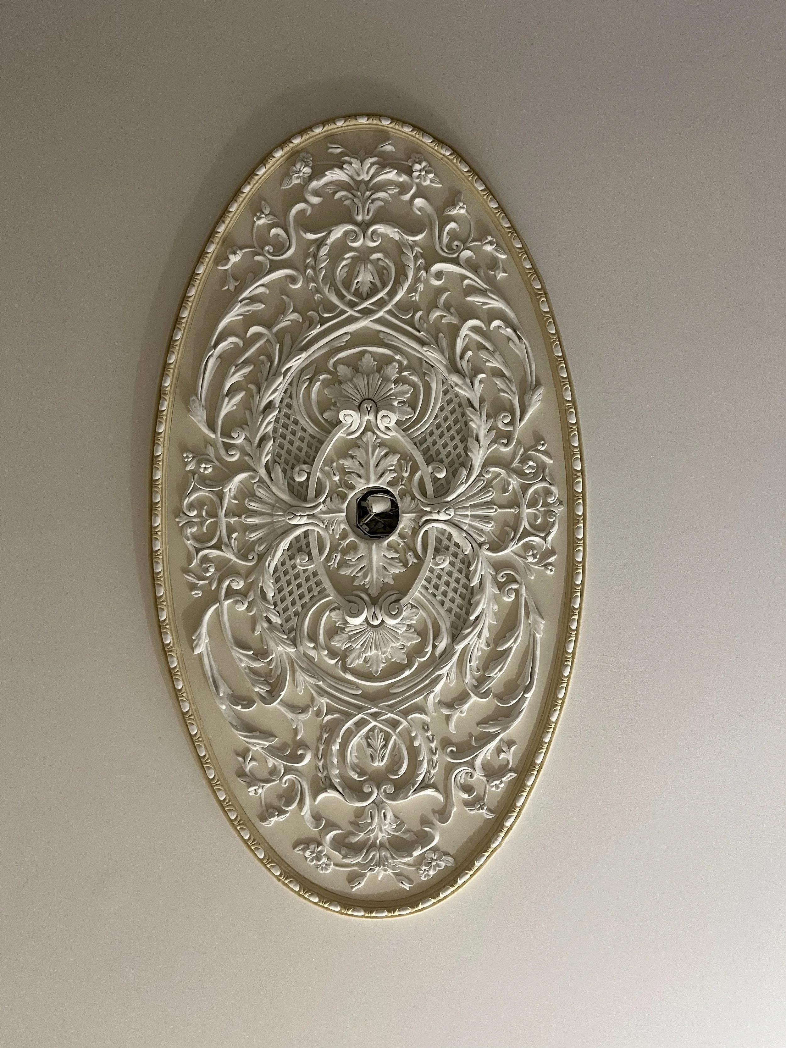 Ornate white ceiling medallion with intricate floral and scroll designs surrounding a central light fixture opening.