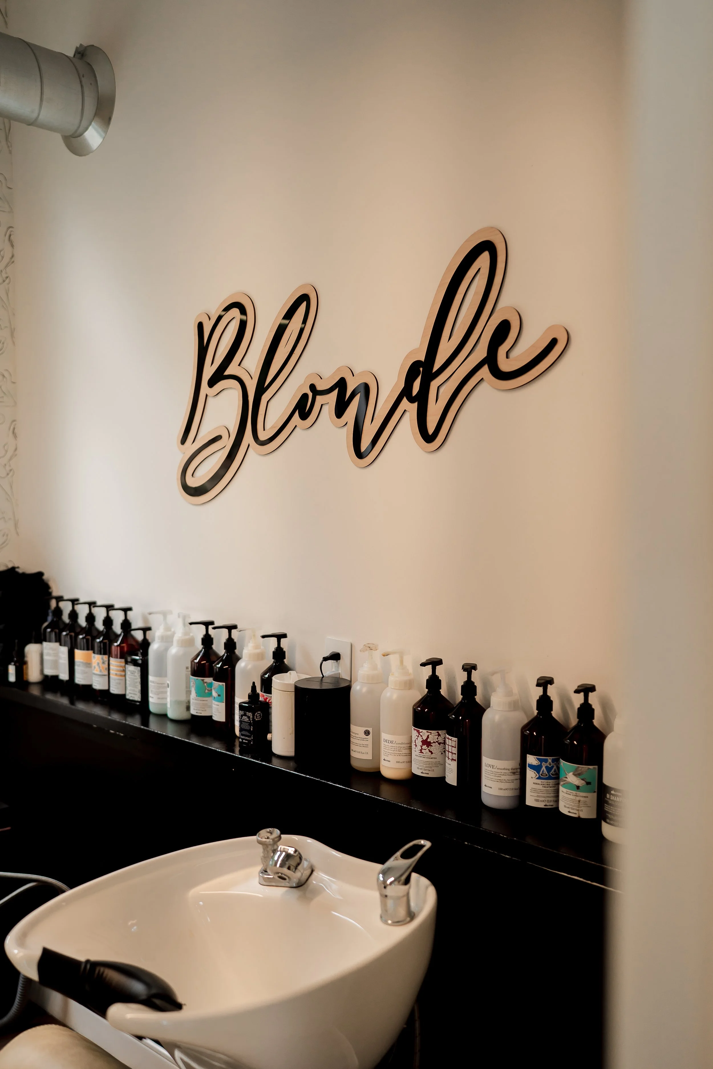 Salon sink with array of bottles and a wall sign that reads 'Blonde' in cursive.
