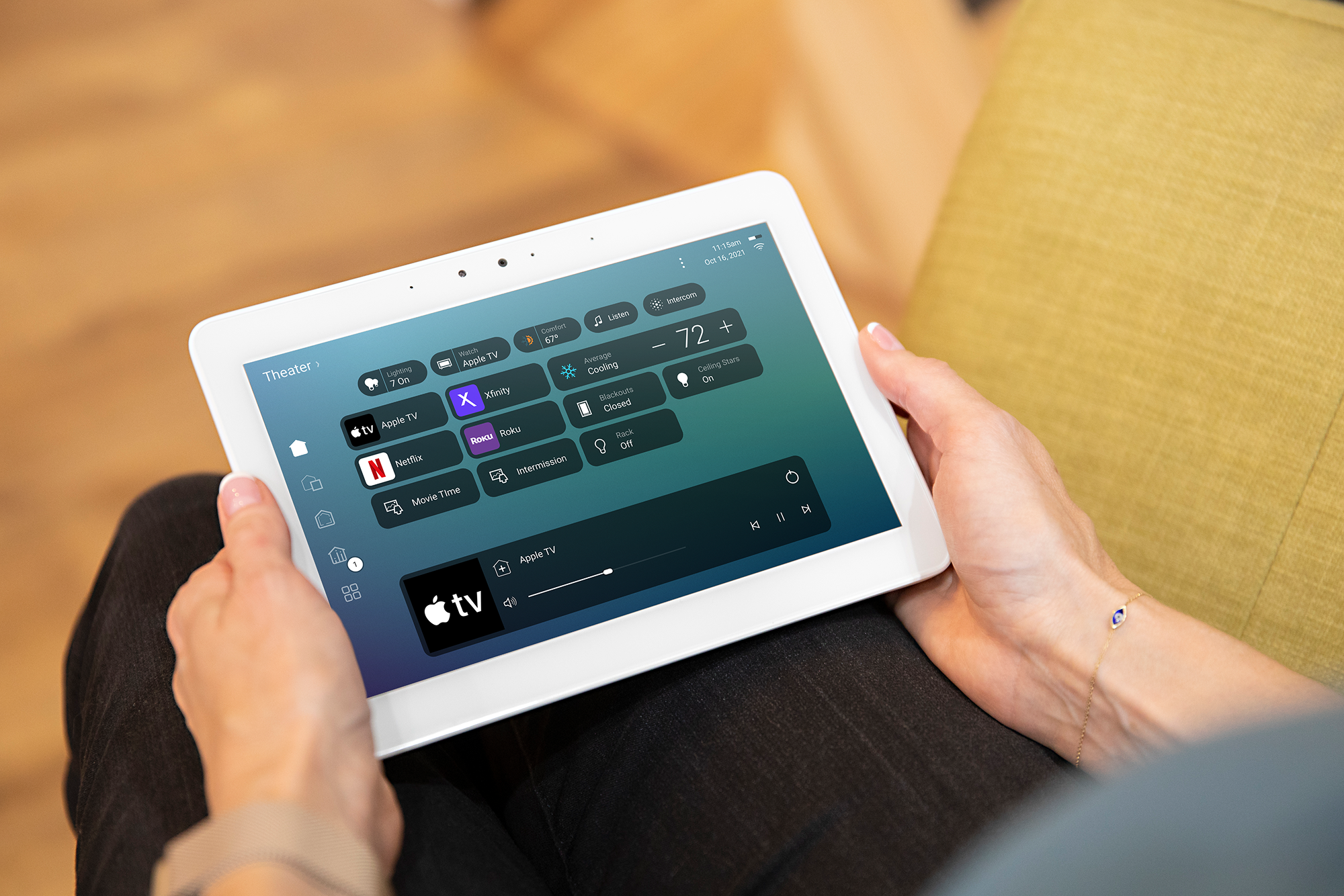 Person holding a white tablet with a home automation control screen displaying options for TV, streaming services, lighting, climate, and other smart devices