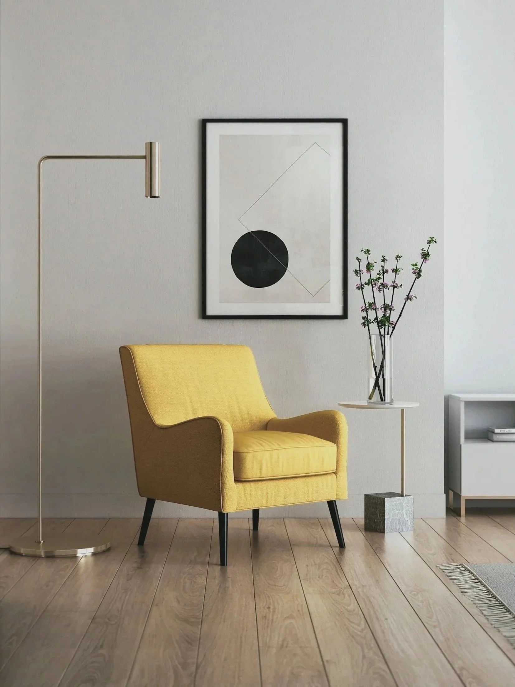 A living room corner with a yellow armchair, a floor lamp, a framed geometric art piece, a small white side table with a flower vase, and a gray and white striped rug on a wooden floor.