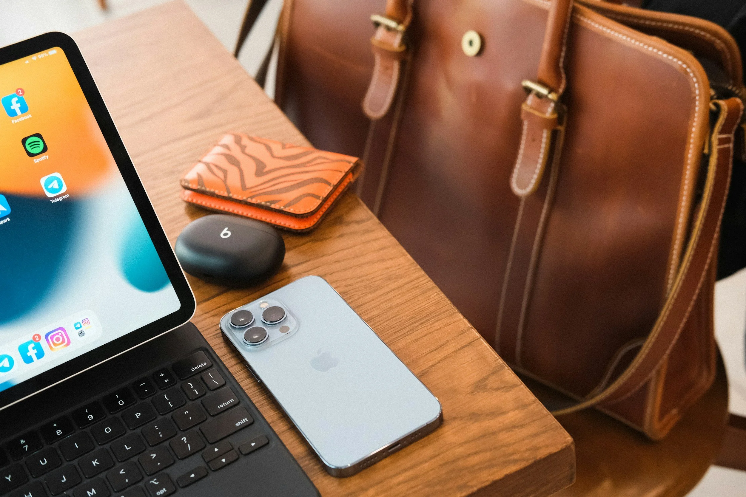 part of a laptop next to a mobile phone on a table with a case for ear pods, a wallet, and a handbag nearby