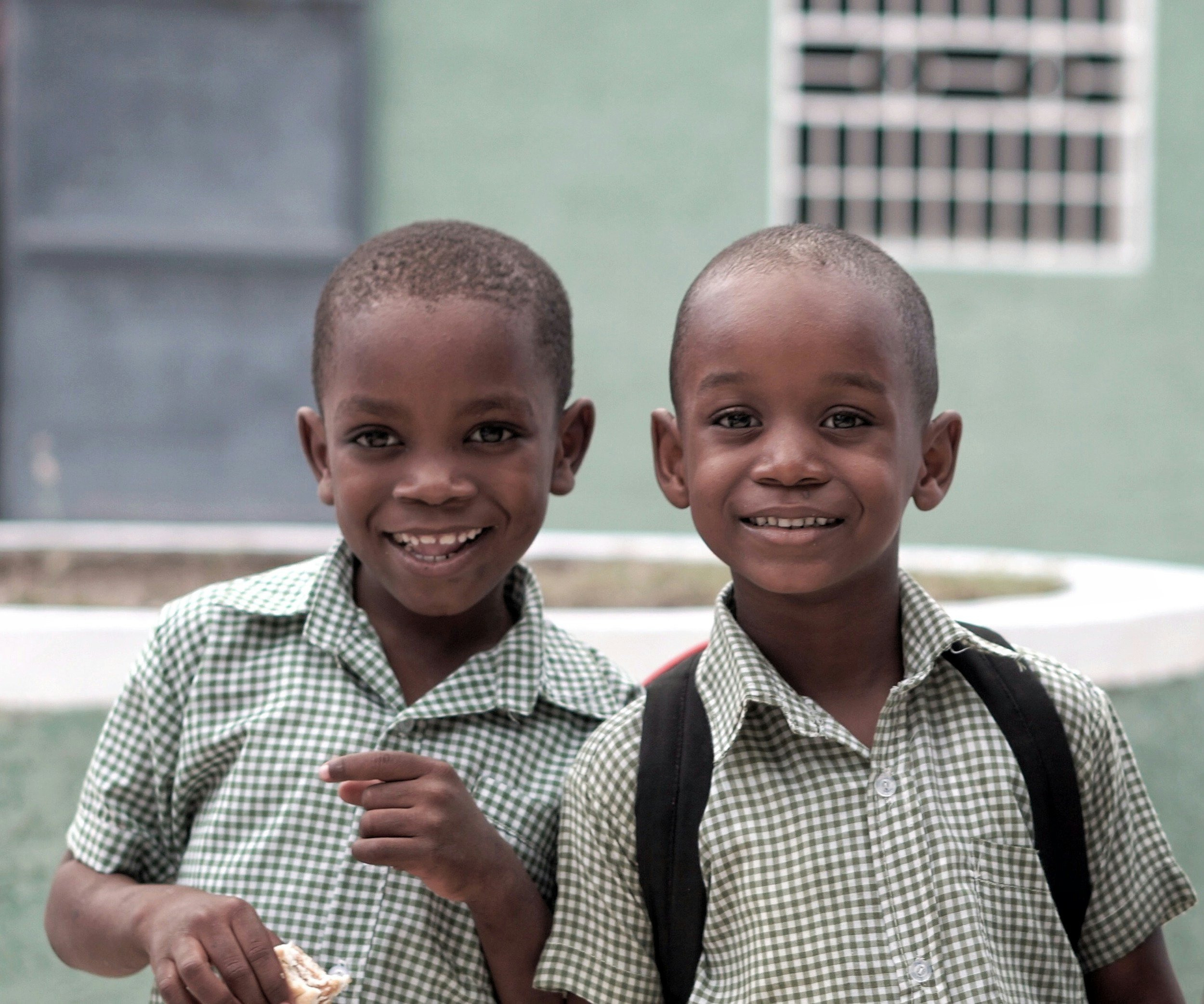 Two young boys in school uniforms smiling outdoors.
