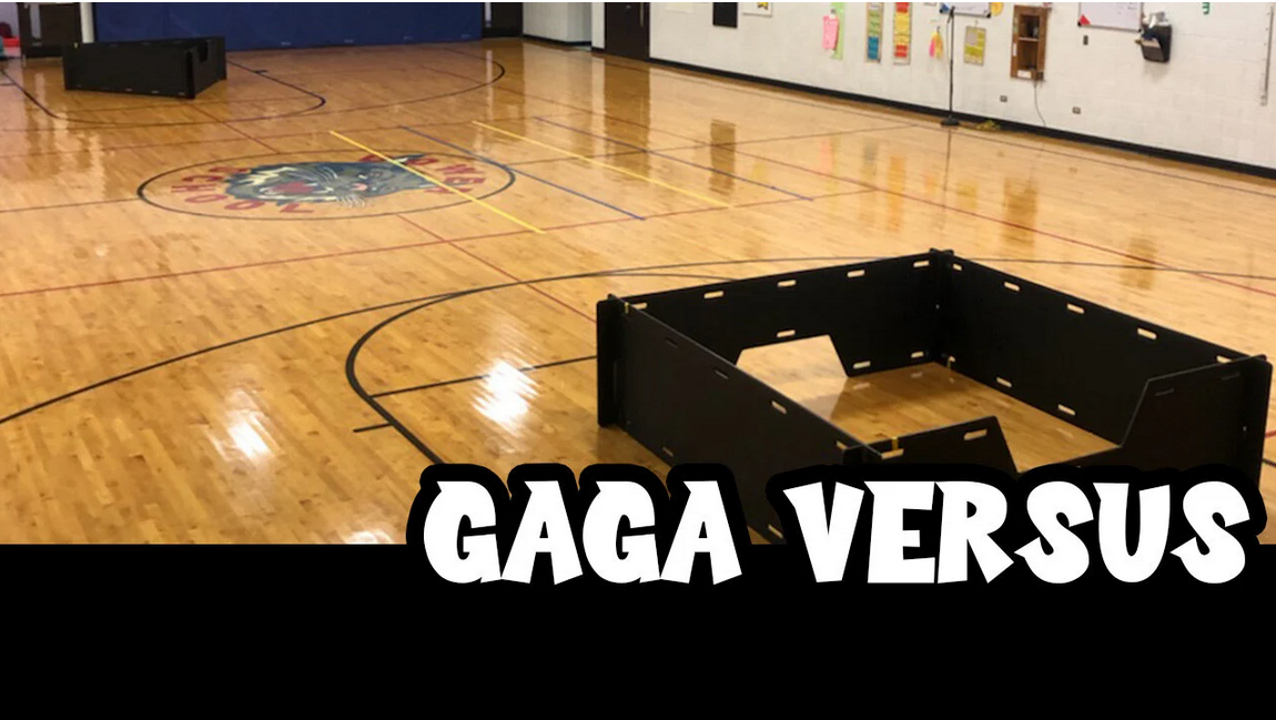 An empty basketball court with a wooden floor, a blue wall, and chairs or equipment against the wall. The court has a logo in the center and lines for basketball. There is a black structure in the foreground, and the text 'GAGA VERSUS' is overlaid at