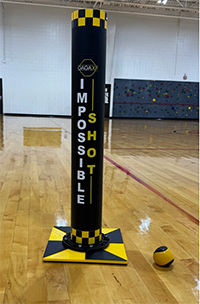 Black and yellow cylinder labeled GagaXP Impossible Shot in gymnasium setting on wood floor