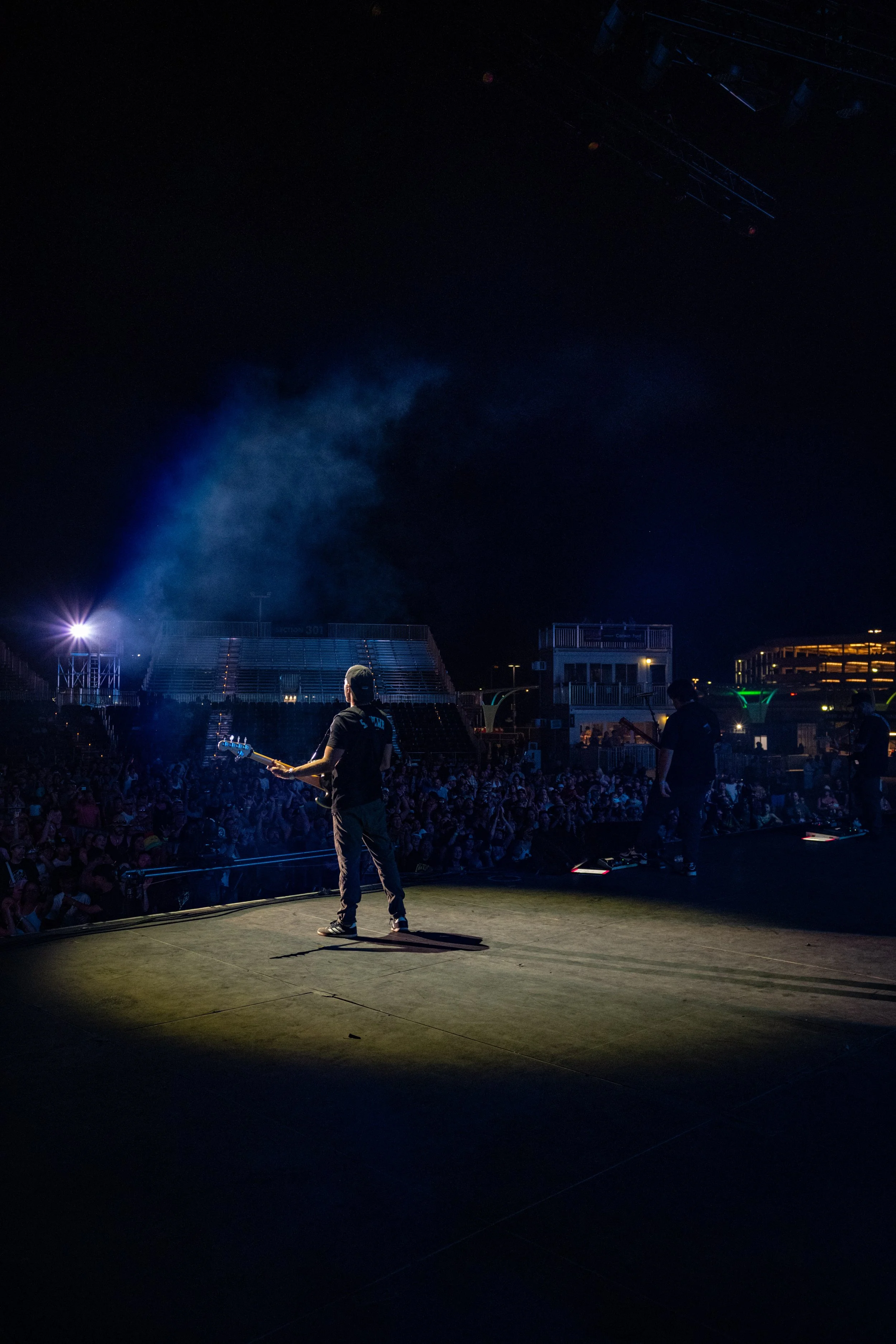 Musicians performing on an outdoor stage at night with a large audience in attendance.