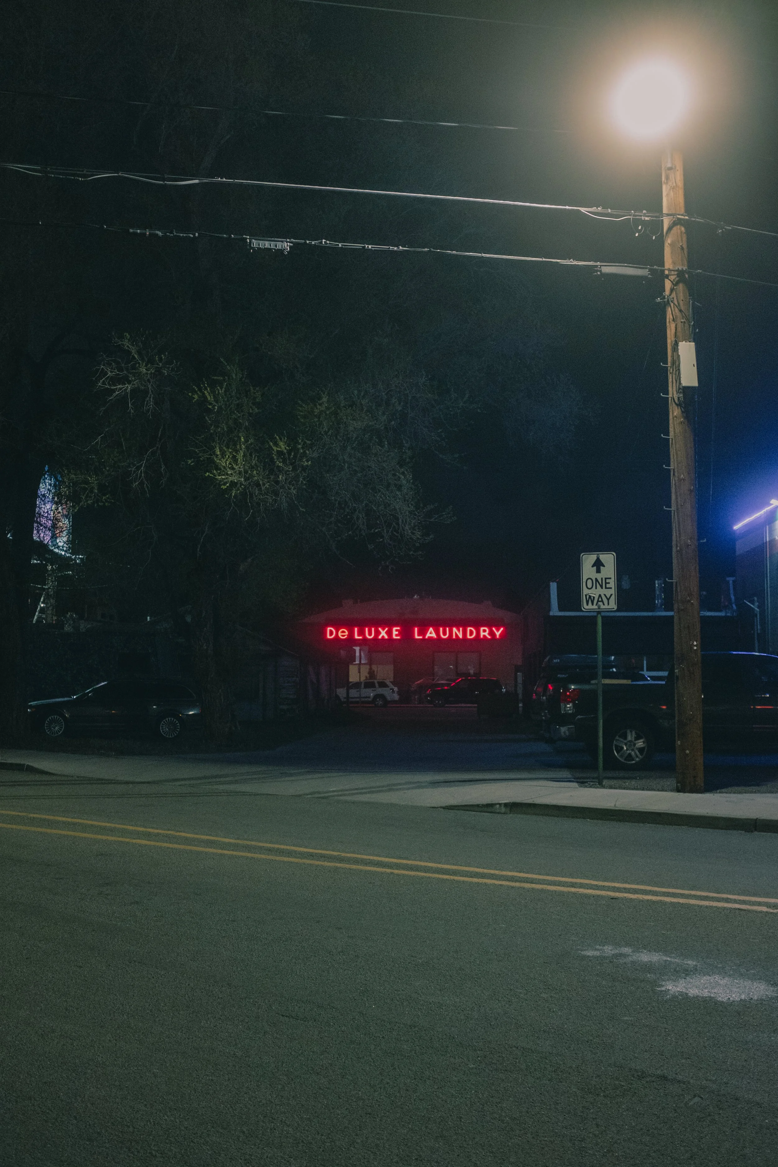 Nighttime street view with a red neon sign that reads 'DeLUXE LAUNDRY' and a one-way street sign.