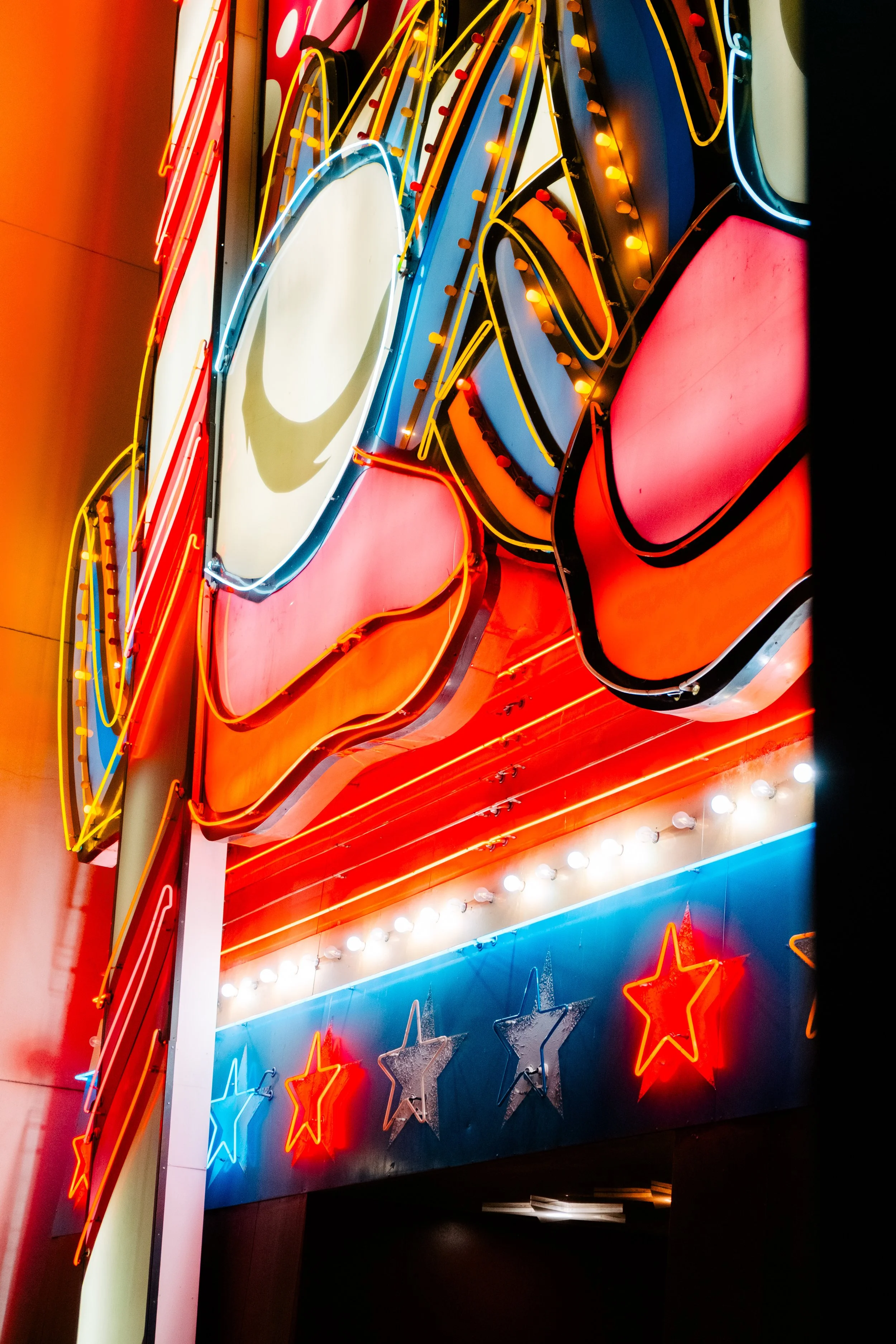Neon sign with red, blue, yellow, and white lights, featuring stars and a large red shape, likely part of a signage for a business or entertainment venue.