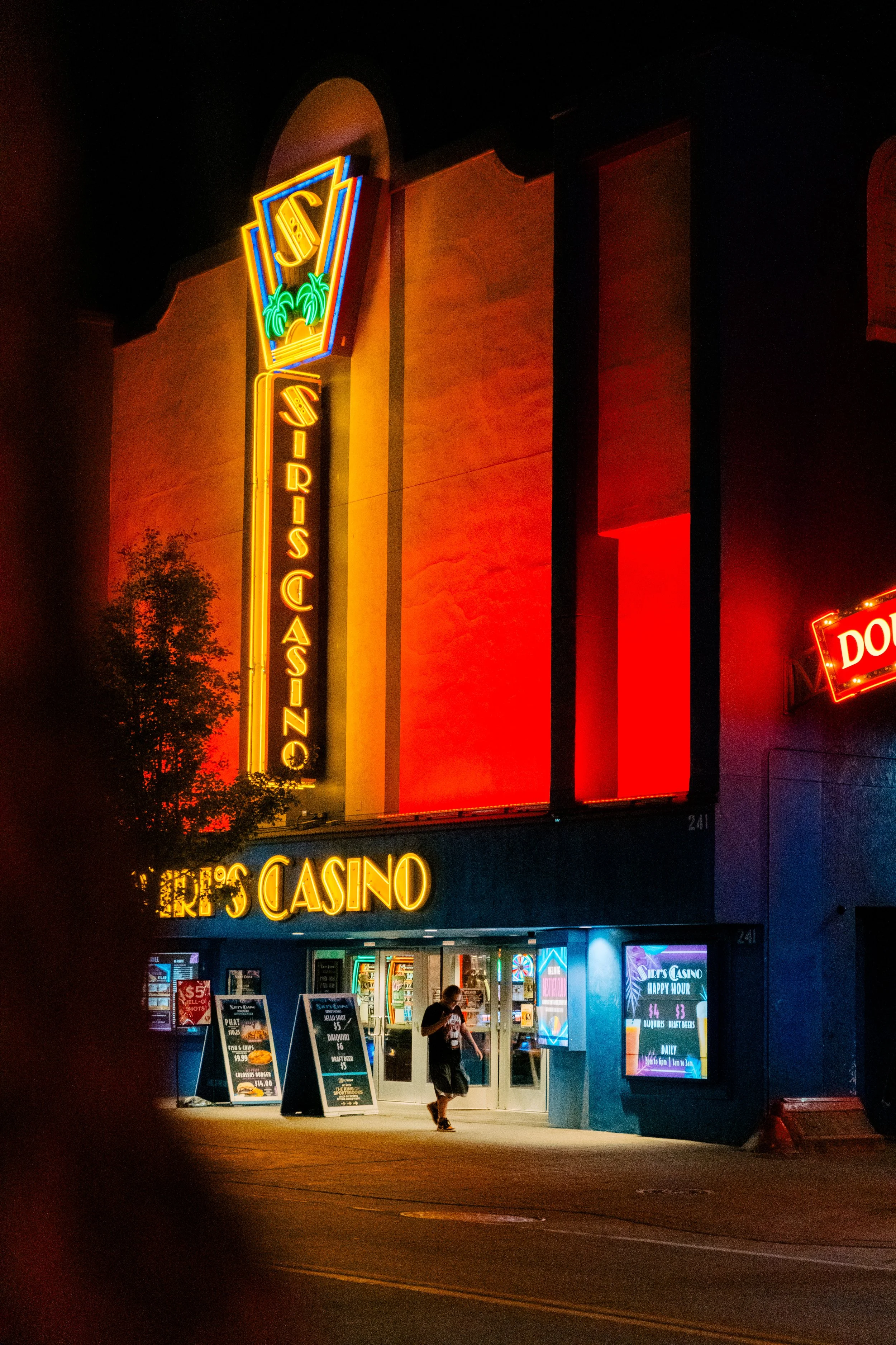 Night view of Caesar's Casino with neon signs and illuminated entrance, a person walking in front of the entrance.