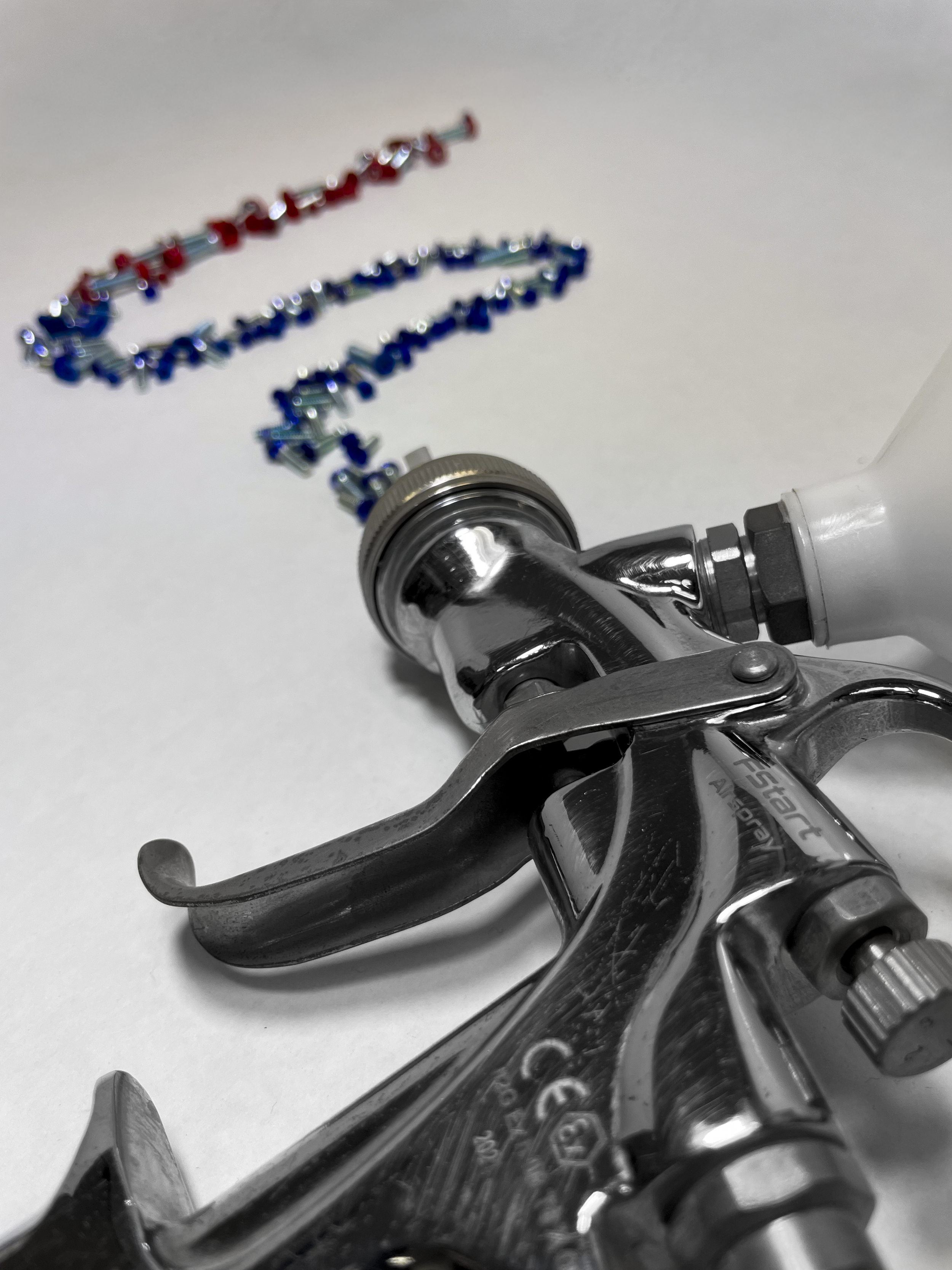 spray painting gun with bright blue and red screws leaving the nozzle