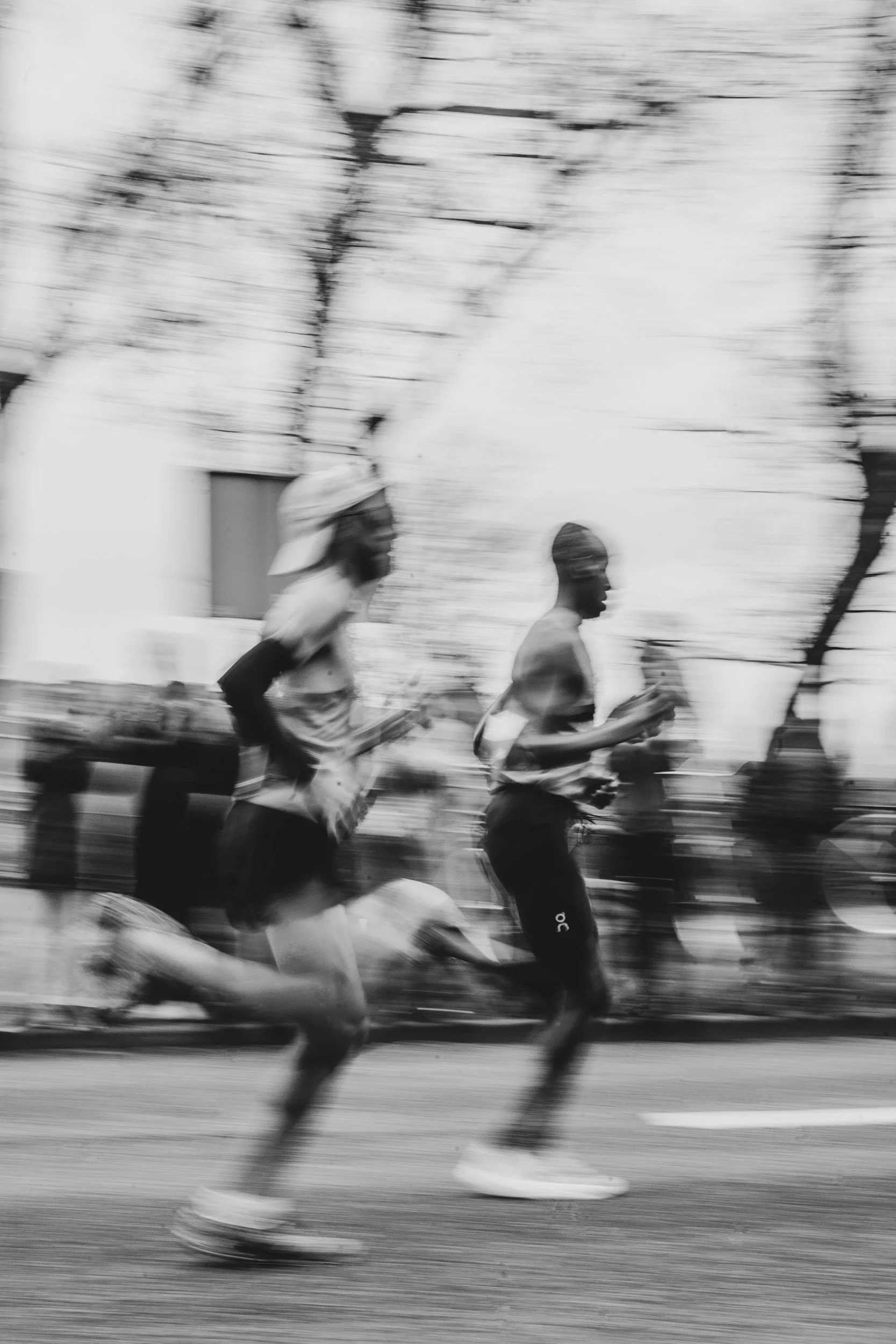 Black and white photo of two marathon runners in motion, with blurred trees and buildings in the background.