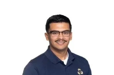 Portrait of a man with glasses, wearing a navy blue polo shirt, smiling against a white background.